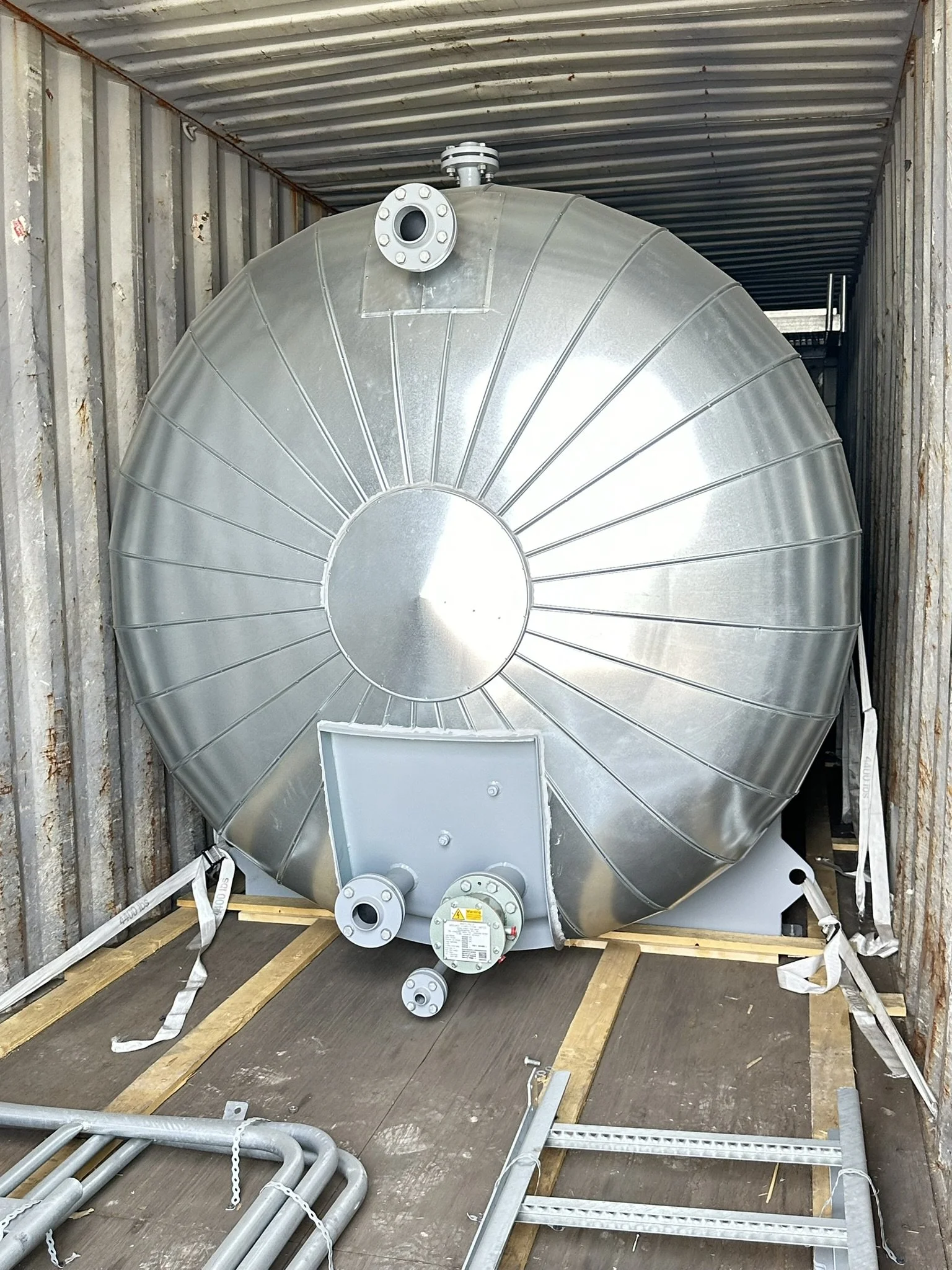 A large cylindrical metal tank with pipes and fittings, installed inside a shipping container or enclosed space.