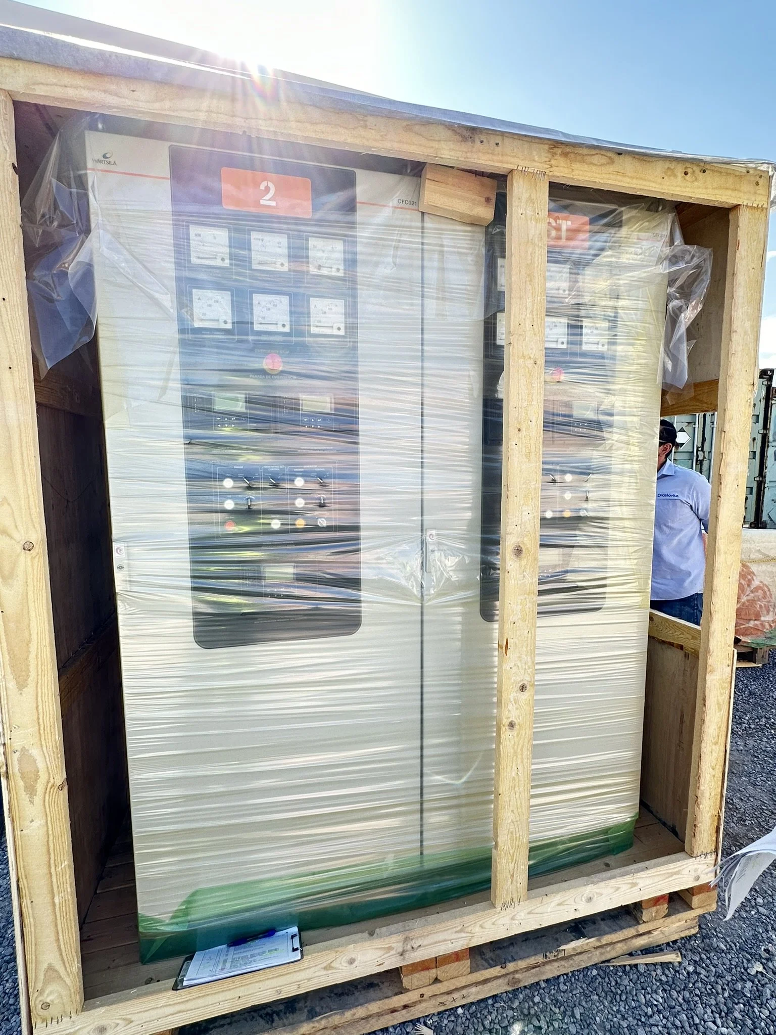 Large vending machine wrapped in plastic and secured in a wooden crate, positioned outdoors under a clear sky.