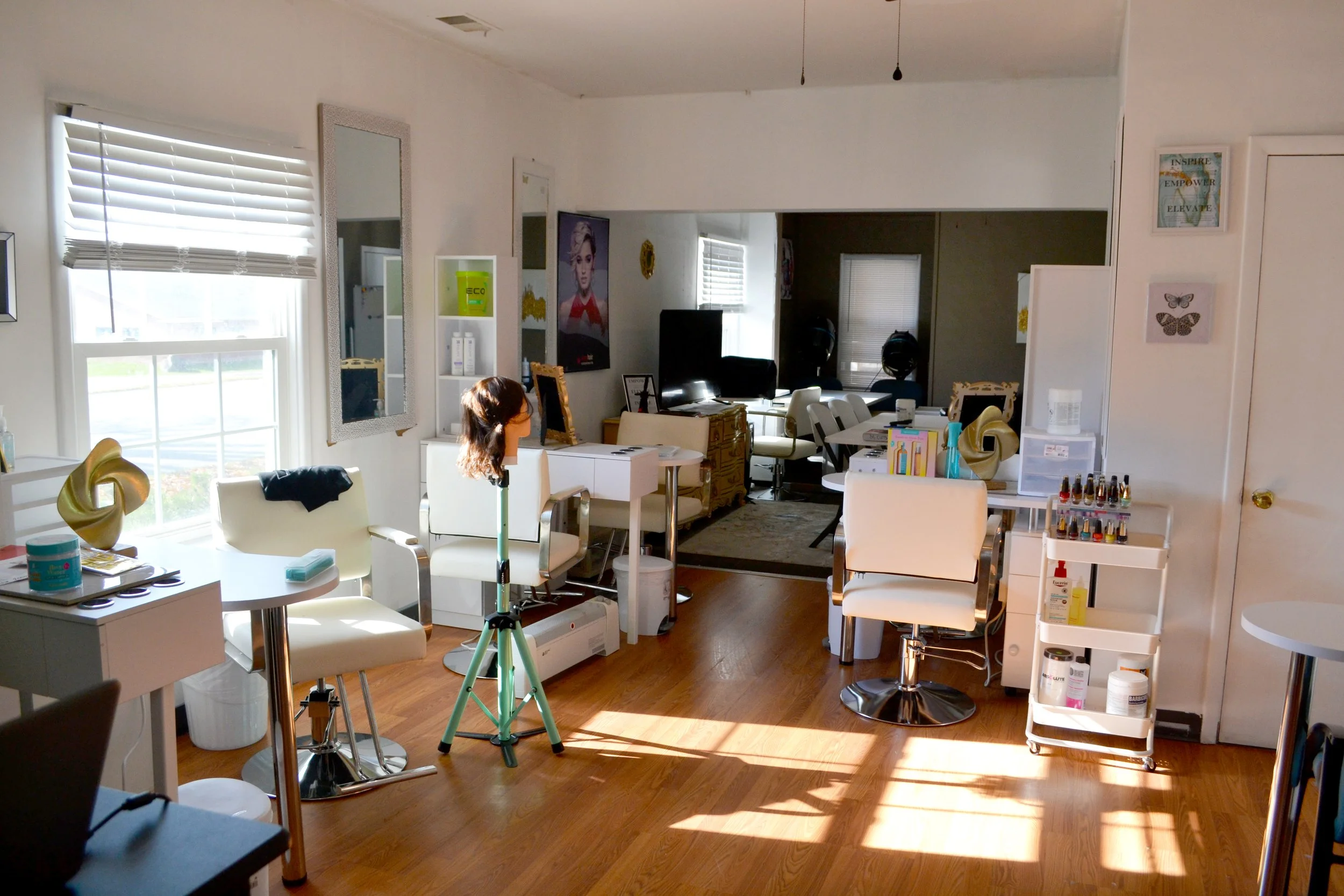 Nail salon with white chairs, manicure station, and nail polish bottles, illuminated by natural light from windows.
