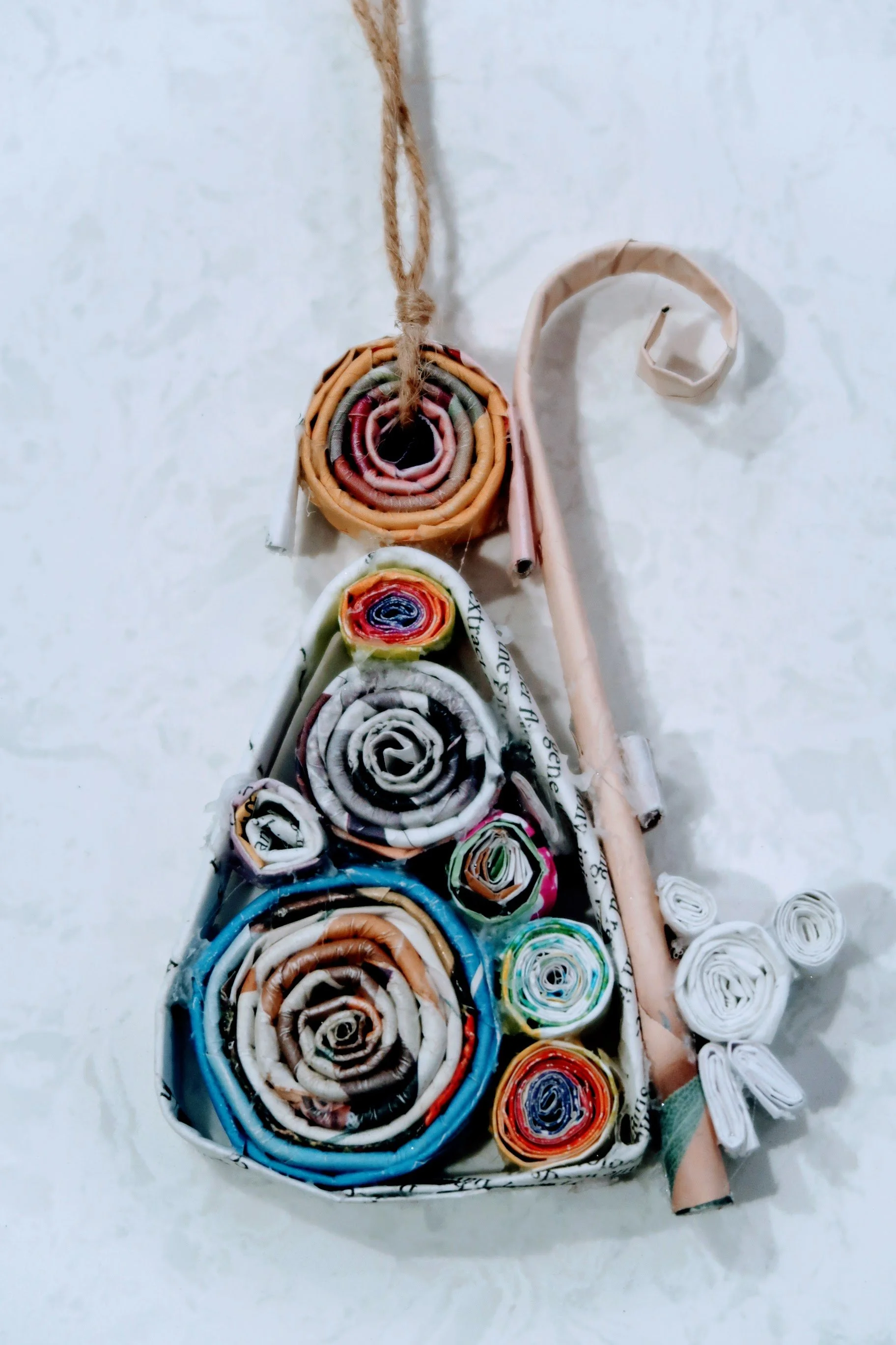 Colorful rolled paper art piece resembling a Christmas tree with a star topper, hanging on a wall.