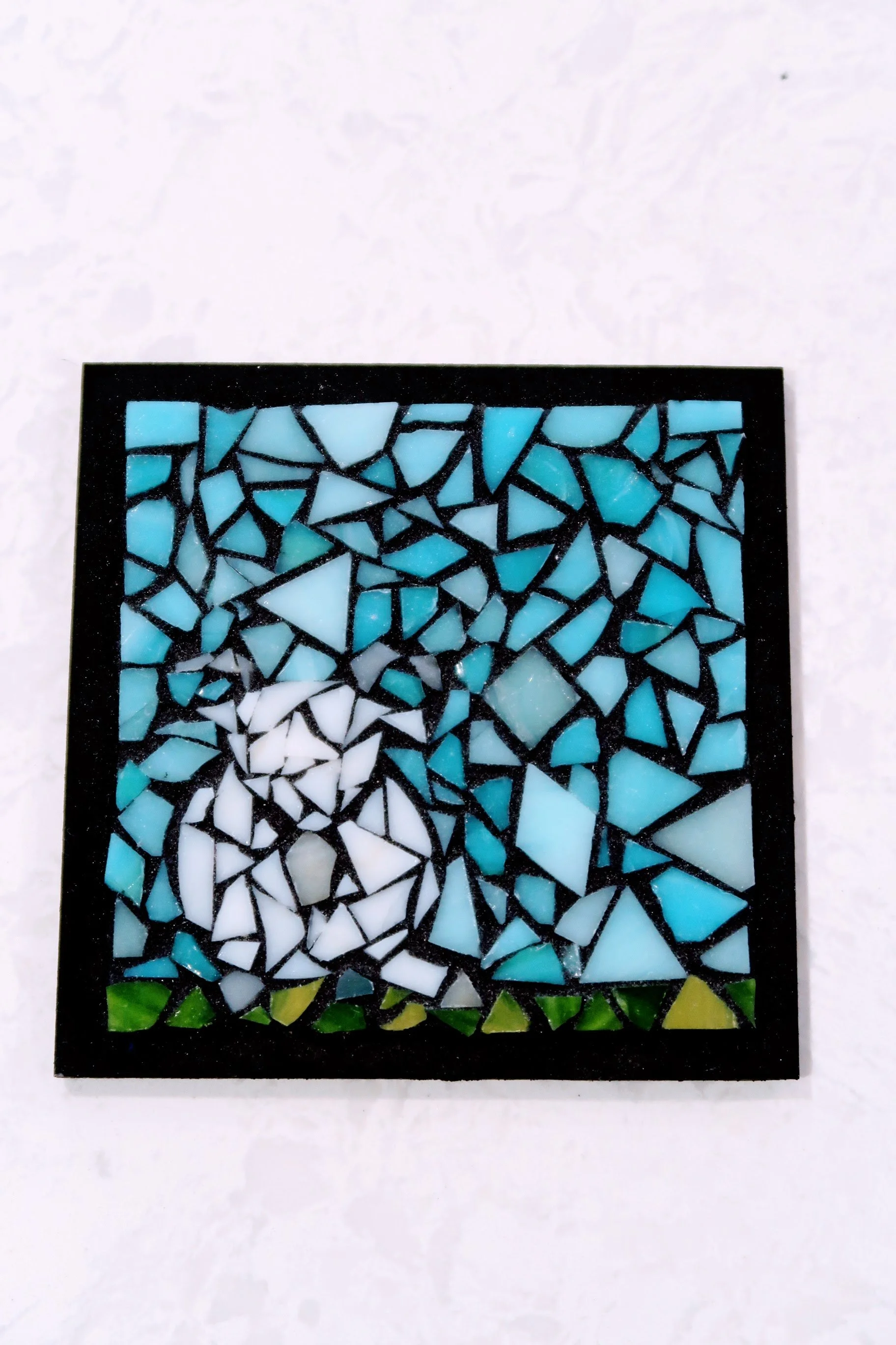 Stained glass mosaic with a landscape scene featuring a sky, clouds, and green grass at the bottom.