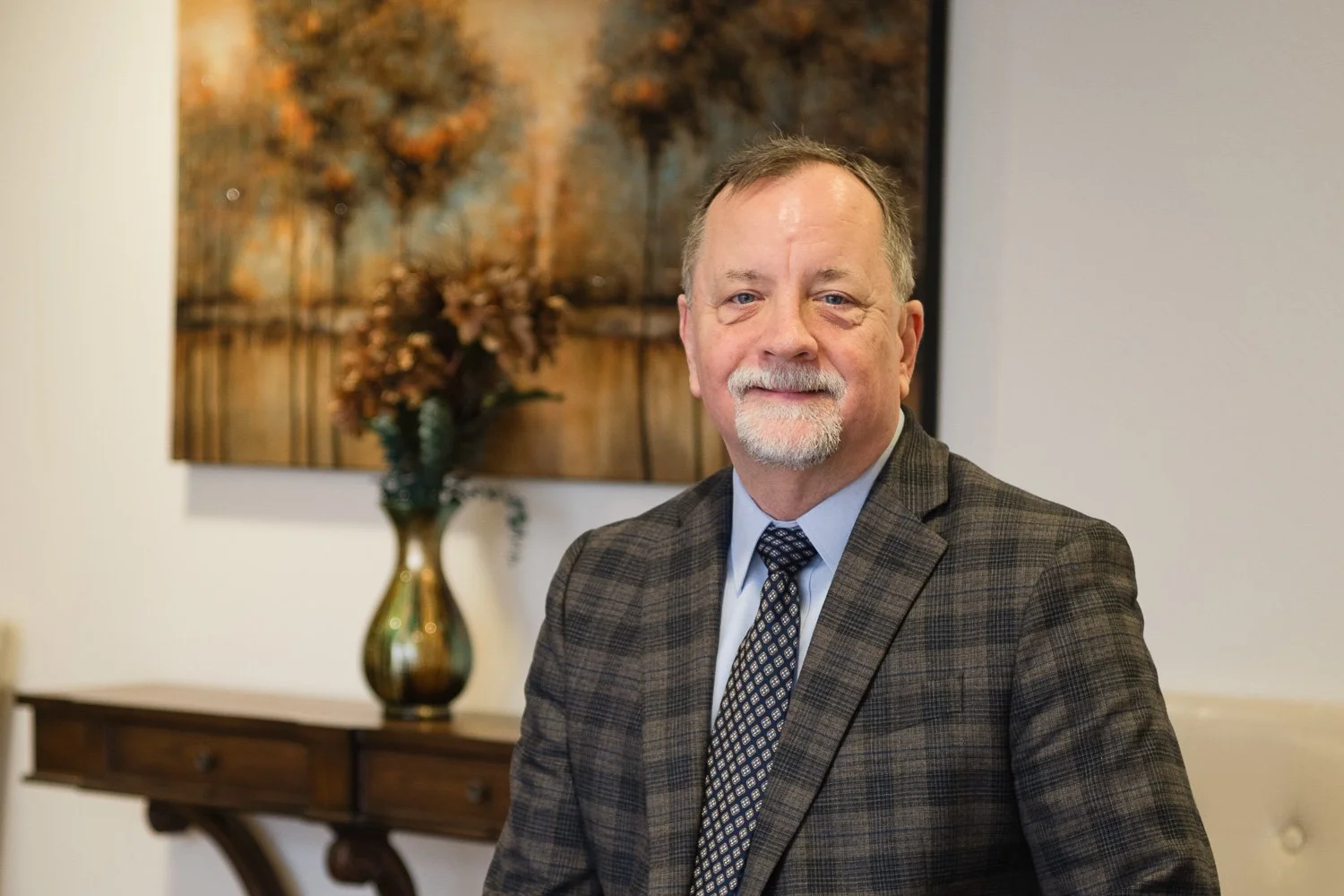 A middle-aged man with a beard and mustache in a suit, posing indoors with a neutral expression