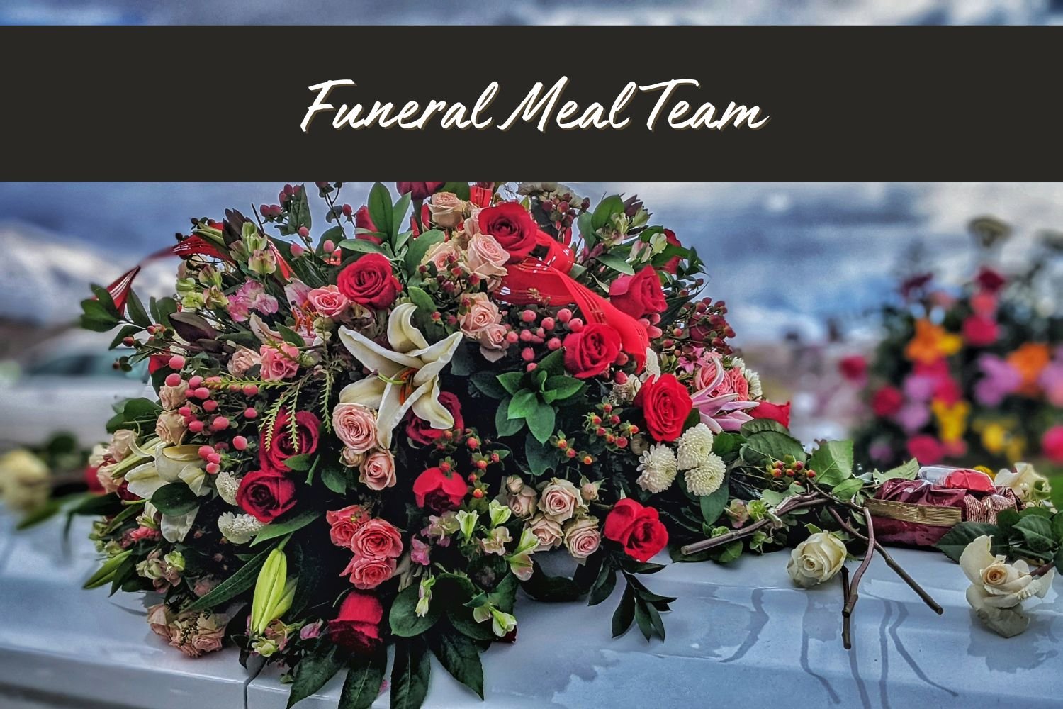 A large floral arrangement with pink, red, white, and purple flowers, including roses and lilies, on a white surface outdoors. The top of the image has a black banner with white text that reads 'Funeral Meal Team'.