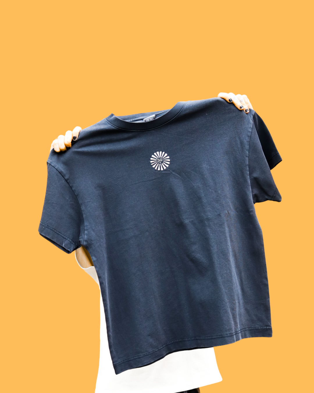 One individual holding up an Empire t-shirt with a small white circular logo on the chest area against a plain orange background.