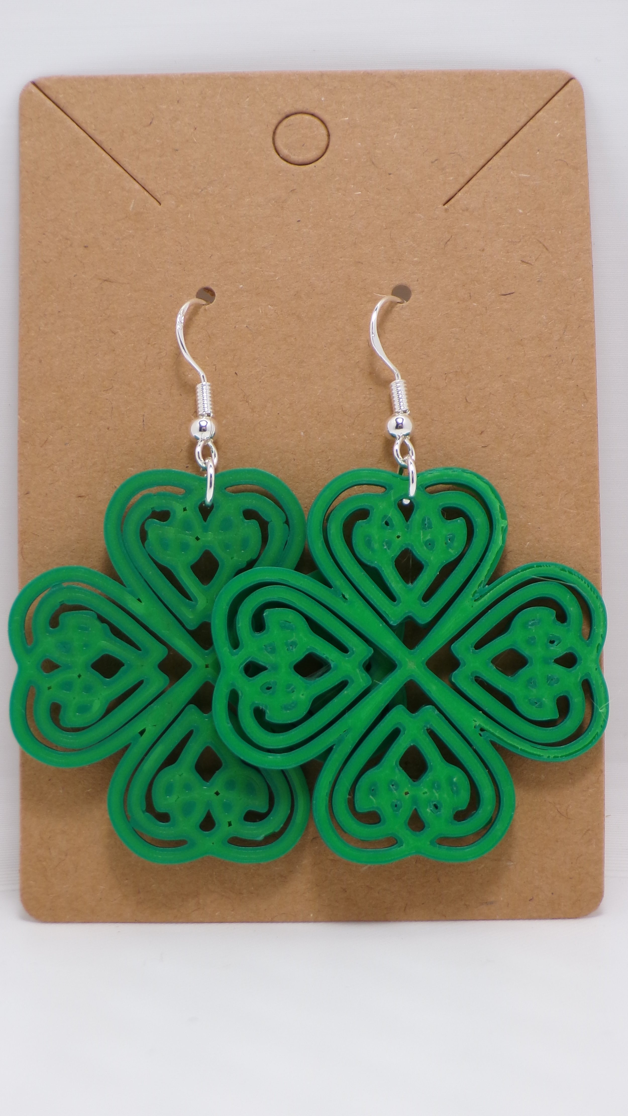 Green shamrock-shaped earrings with intricate cut-out designs hanging on a brown display card.