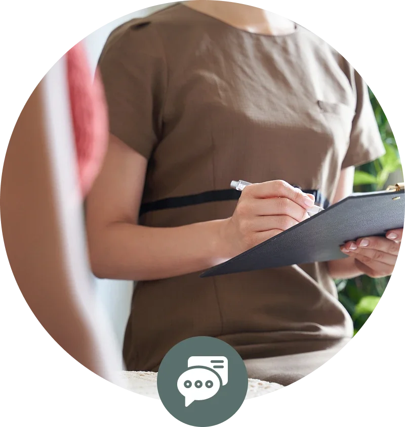 A person in a beige shirt holding a clipboard and writing with a pen, while another person is visible in the foreground.