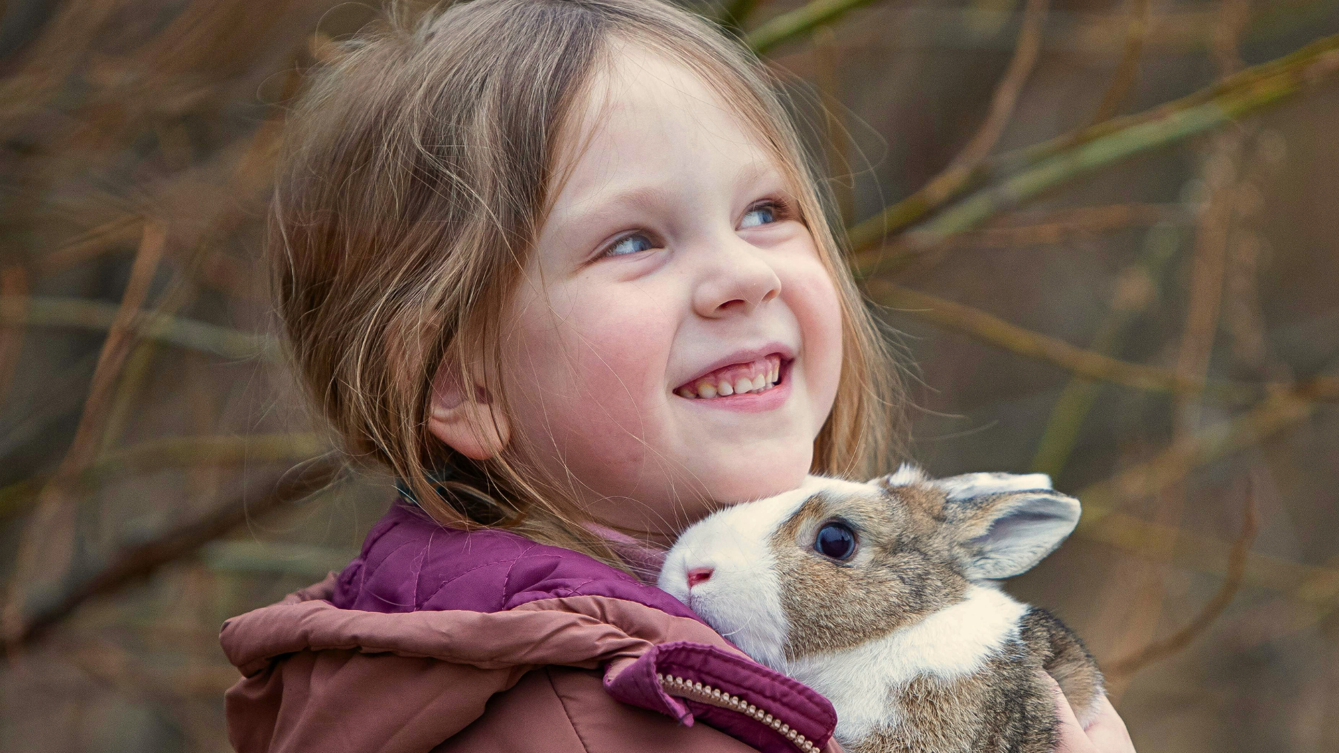 Hymyilevä tytto halailee pientä kania ulkona luonnon keskellä.