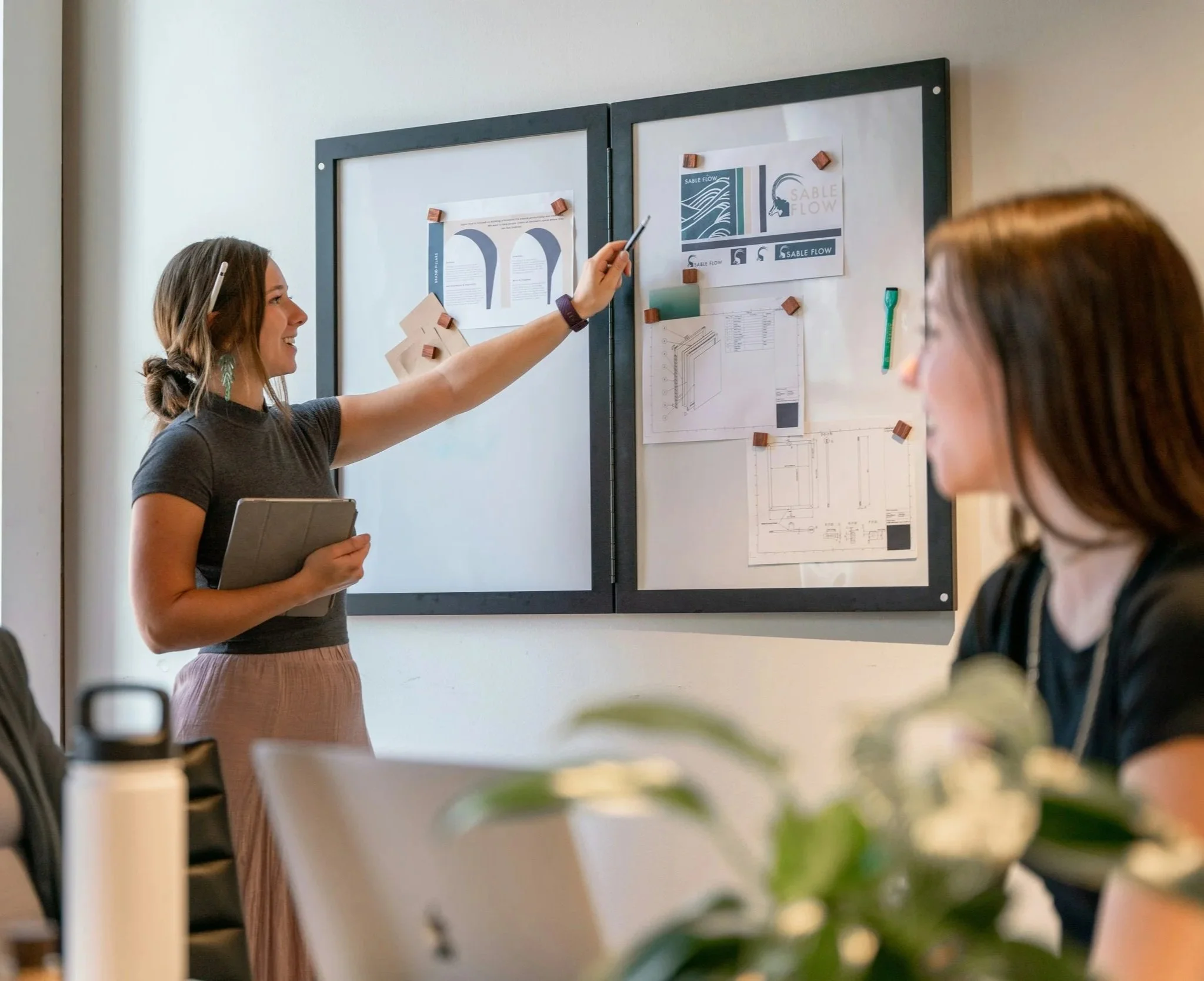 a woman points at a whiteboard in a meeting with colleagues