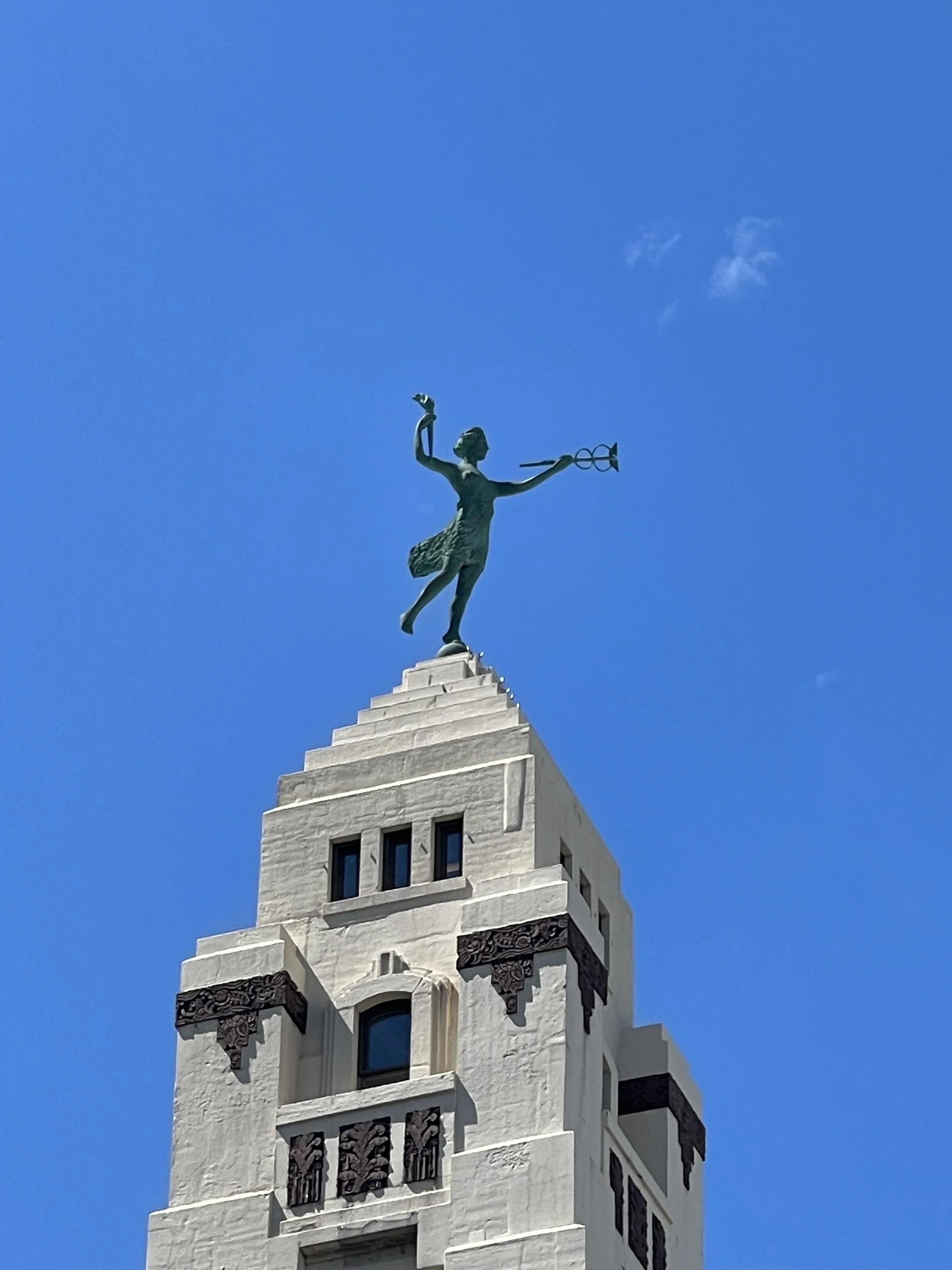 Bronze allegorical statue holding a caduceus atop an Art Deco Chicago landmark beneath a clear blue sky.