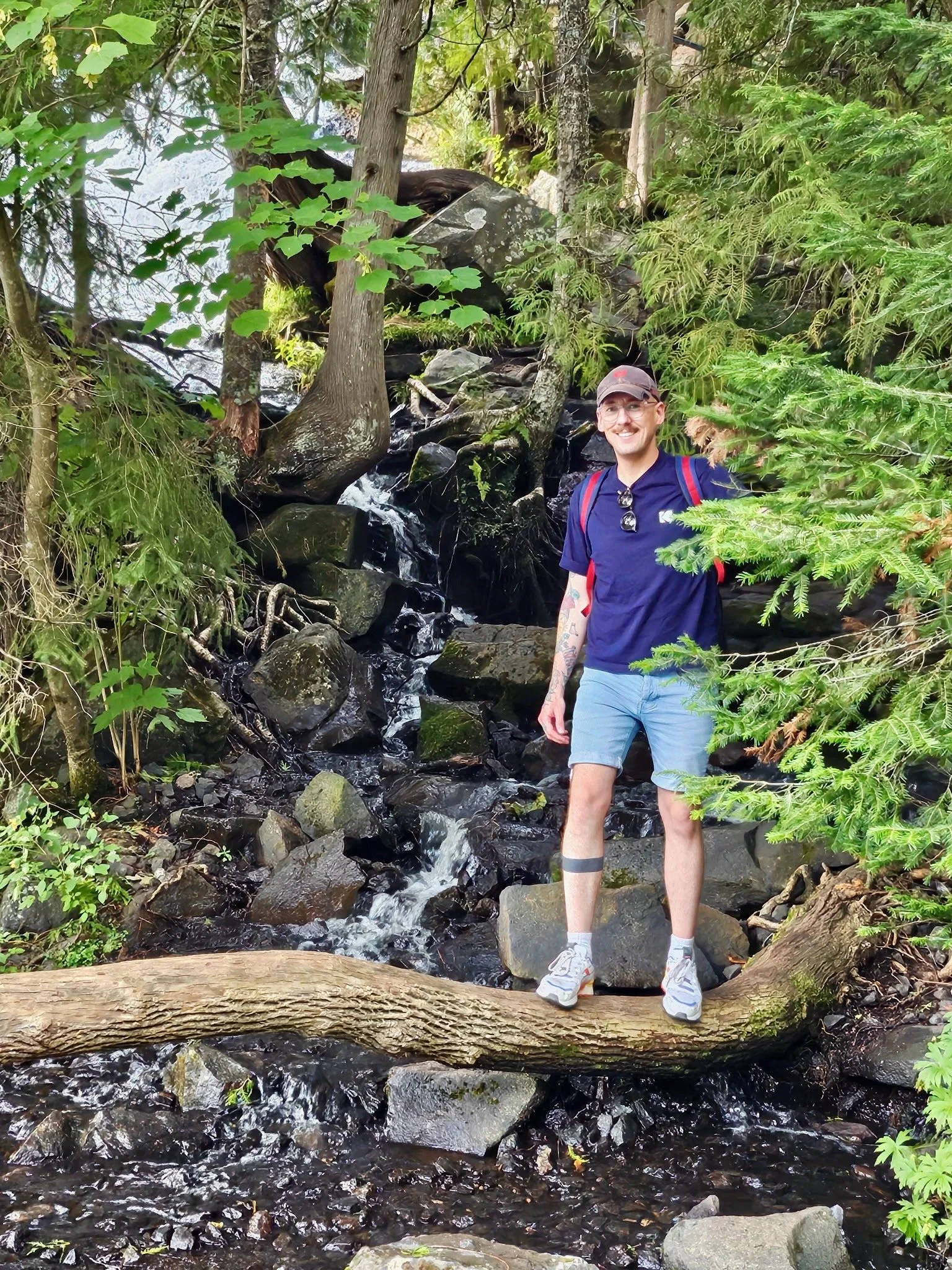 Daniel Karl Nennig standing on a fallen log beside a forest stream.
