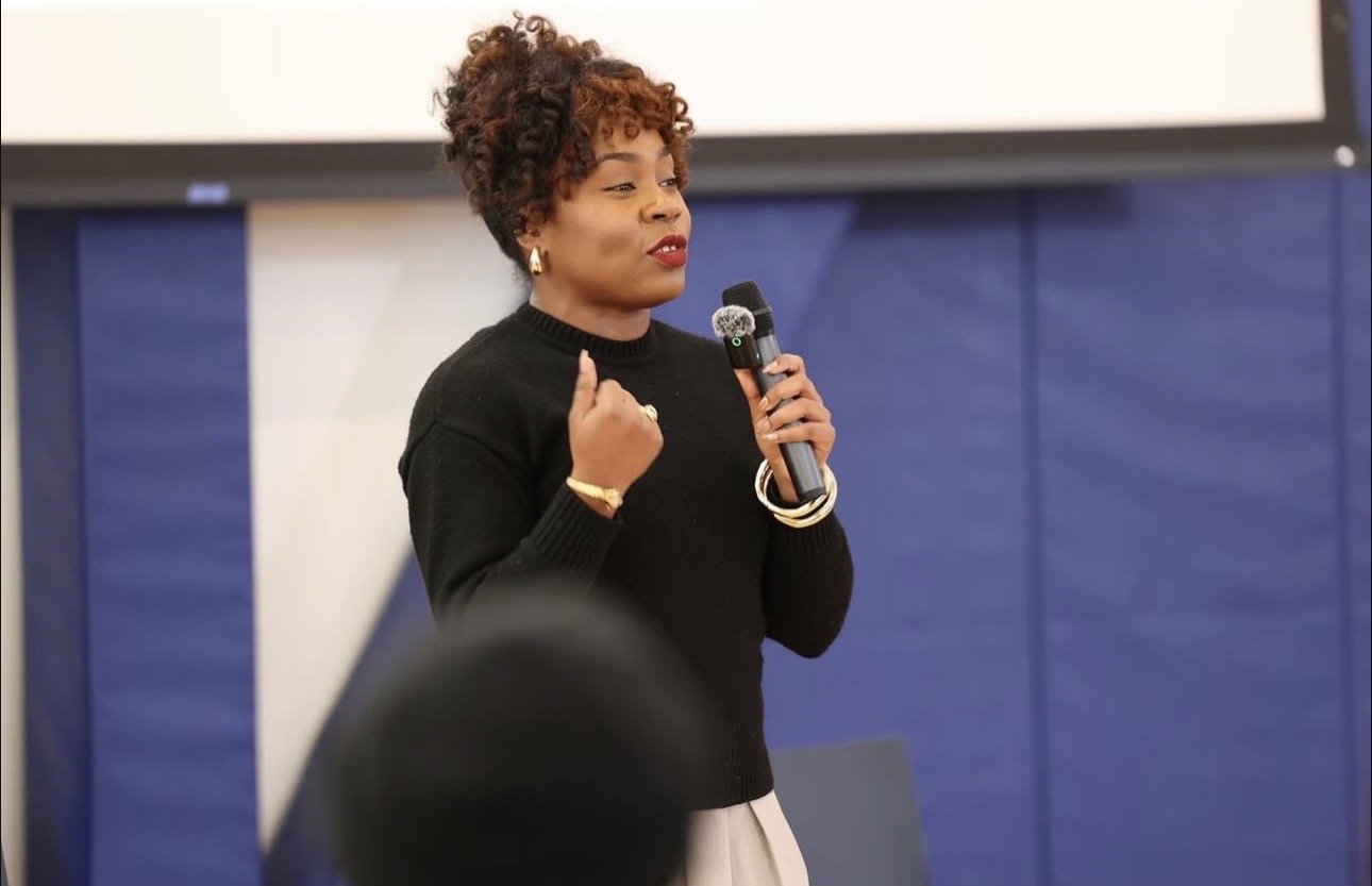 Jessicah Pierre with short curly hair speaking into a microphone during a presentation or speech.
