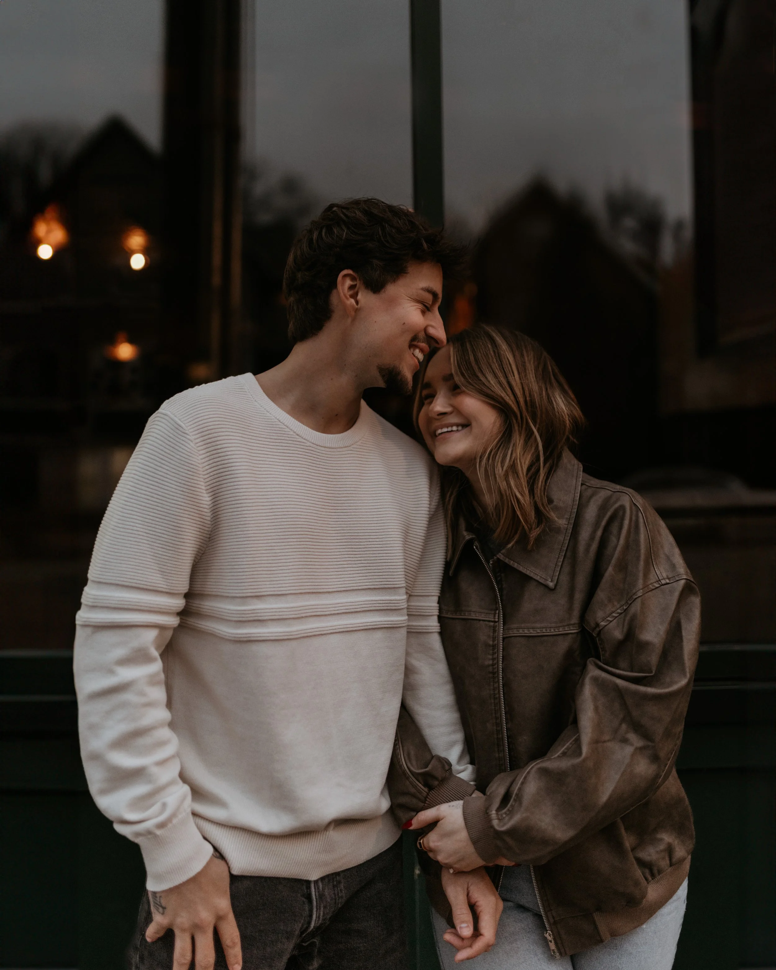A young couple sharing a happy moment outside, standing close to each other, smiling and leaning their heads together.