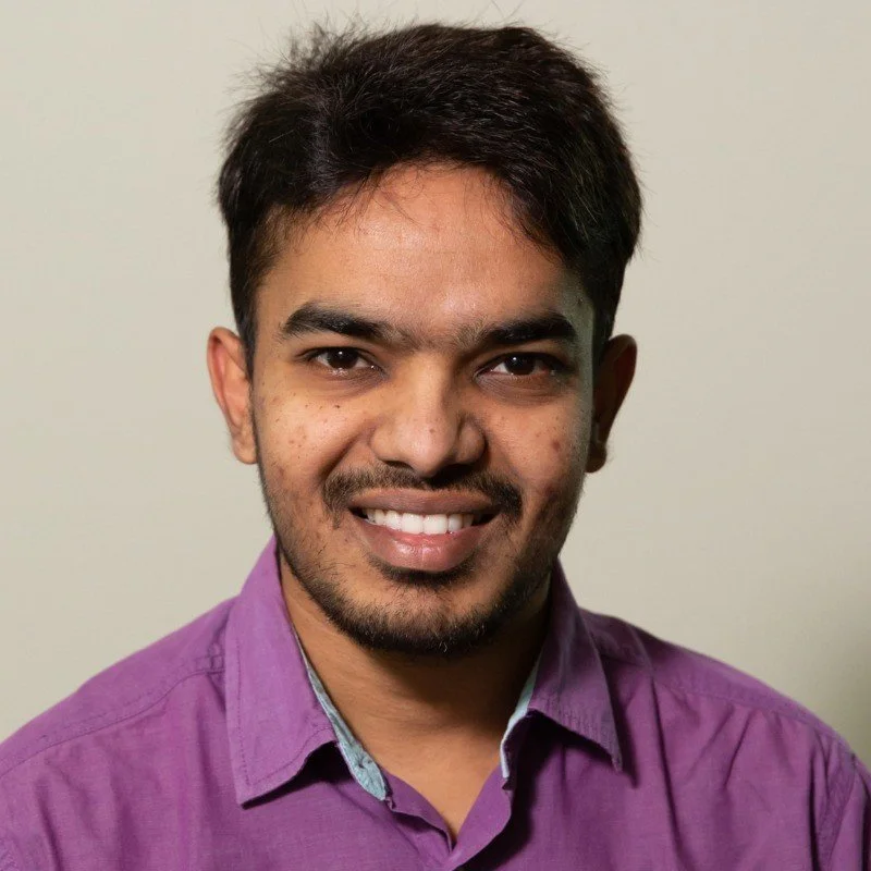 Smiling woman with natural curly hair, glasses, hoop earrings, layered necklaces, and a striped blouse.