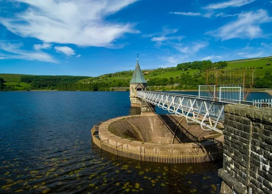 A white bridge over a body of water with green hills in the background and a partly cloudy sky.