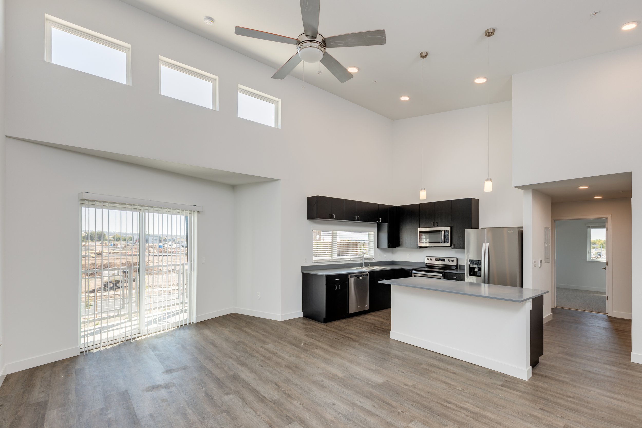 Modern kitchen with black cabinetry, stainless steel appliances, and a kitchen island, in an open-concept living space with high ceilings and multiple windows.