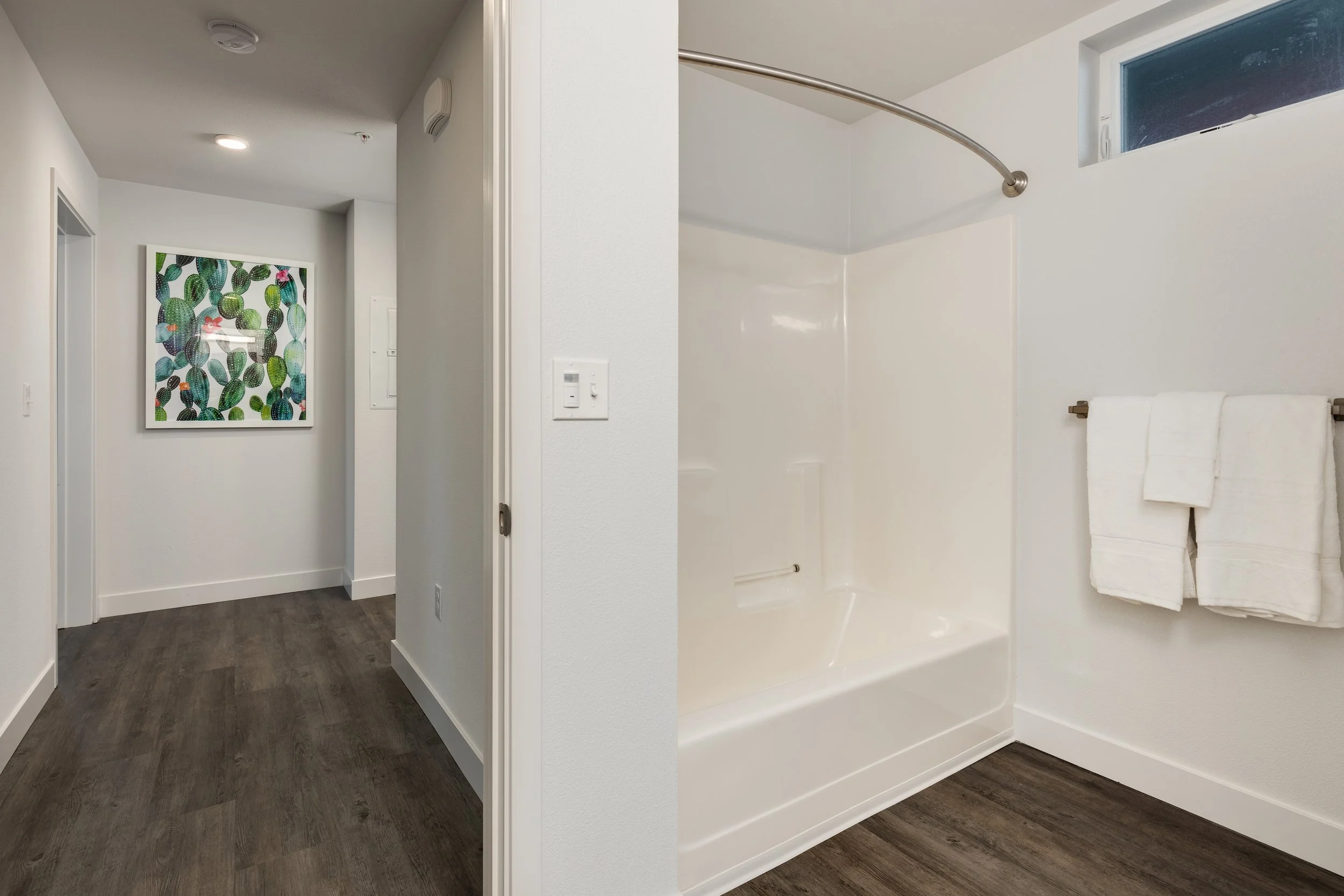A hallway leading to a bathroom with a shower and white towels on a towel rack.