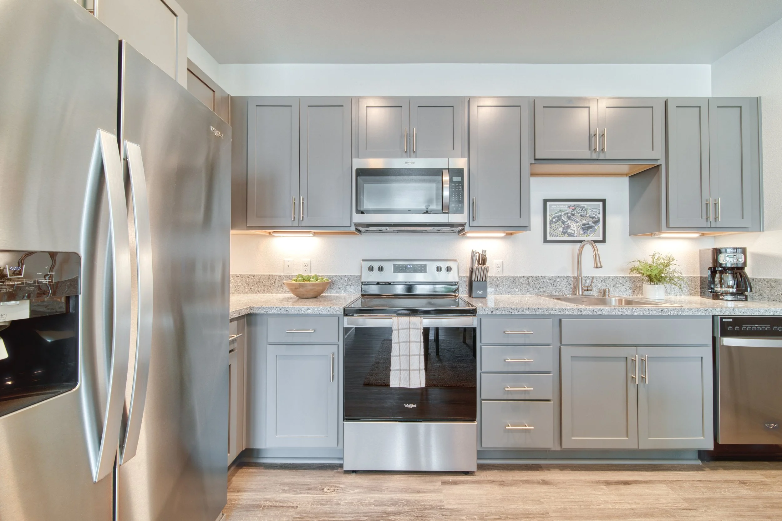 Modern kitchen with gray cabinets, stainless steel appliances, granite countertops, a stove, microwave, coffee maker, and plant decorations.