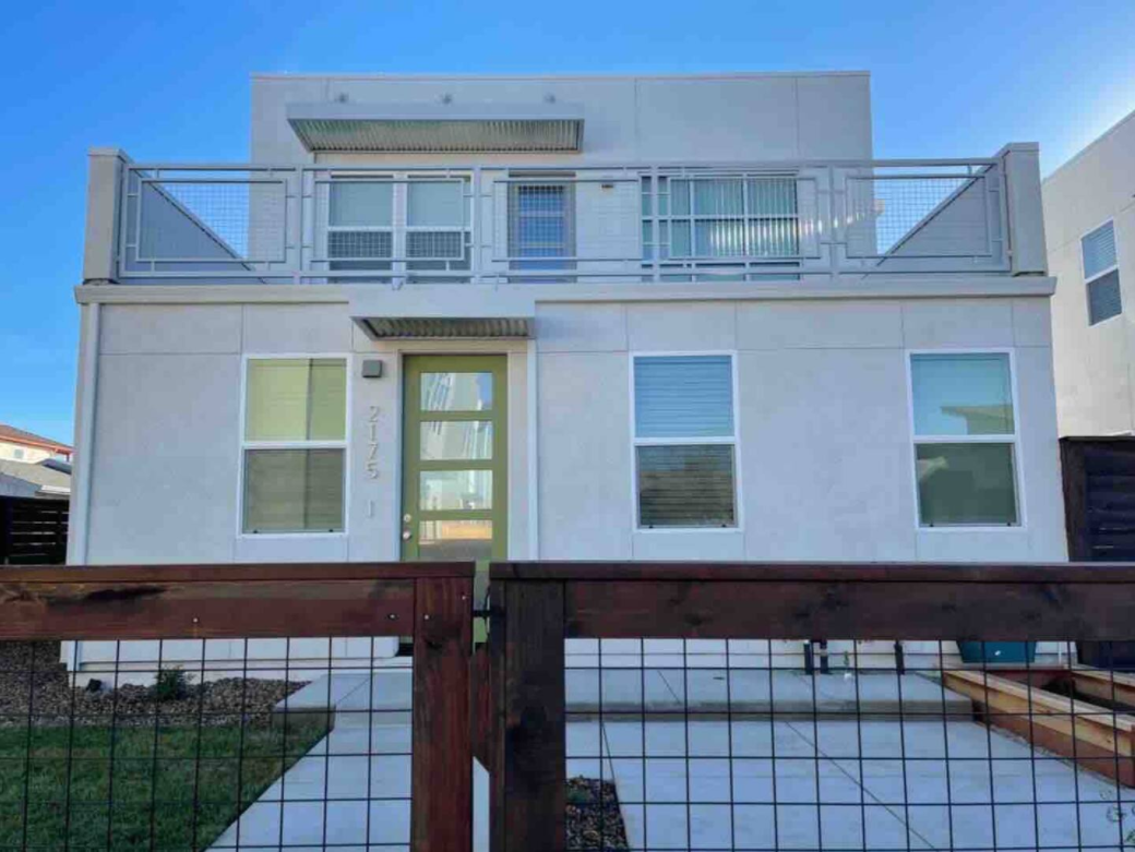Front view of a modern, two-story house with a balcony, white exterior, green front door, and four large windows.