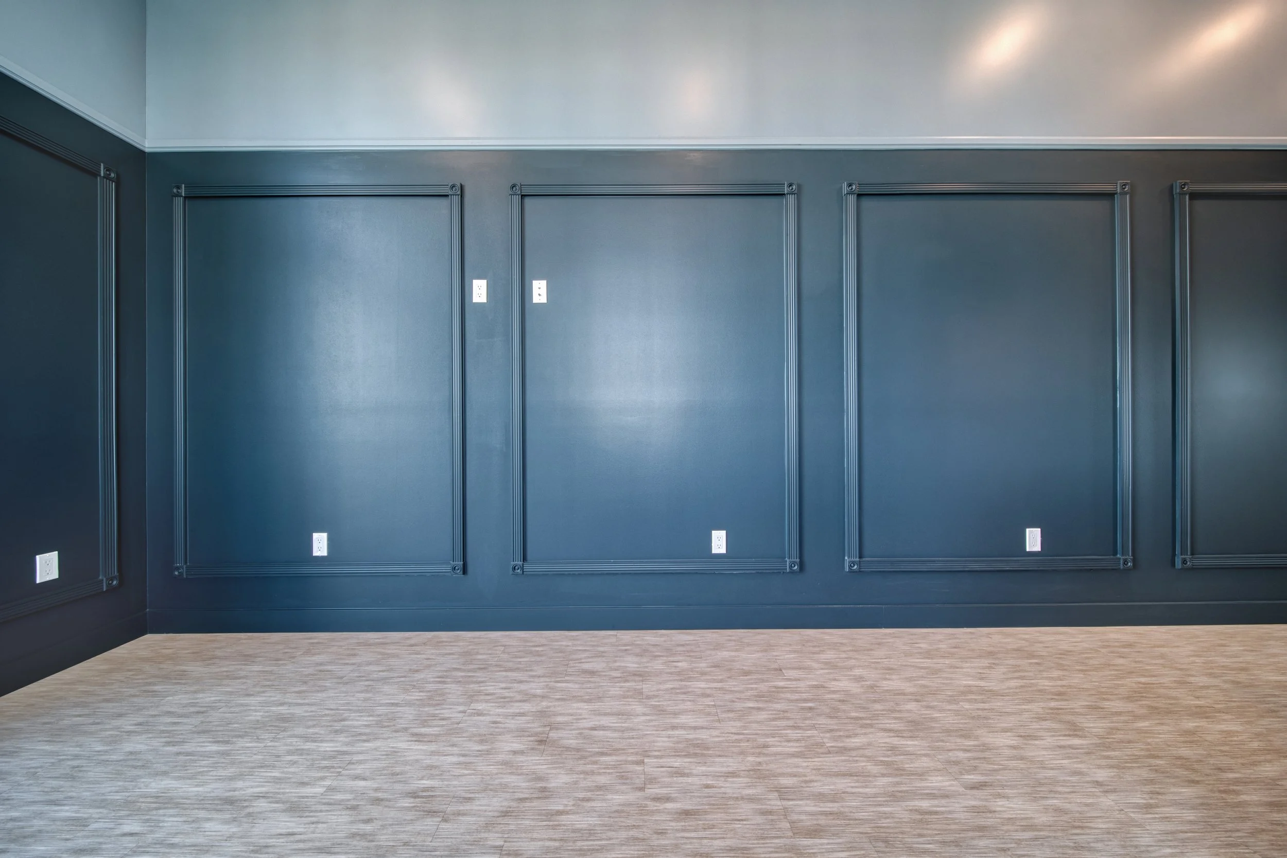 Empty room with dark blue walls, decorative molding, electrical outlets, and light-colored hardwood flooring.