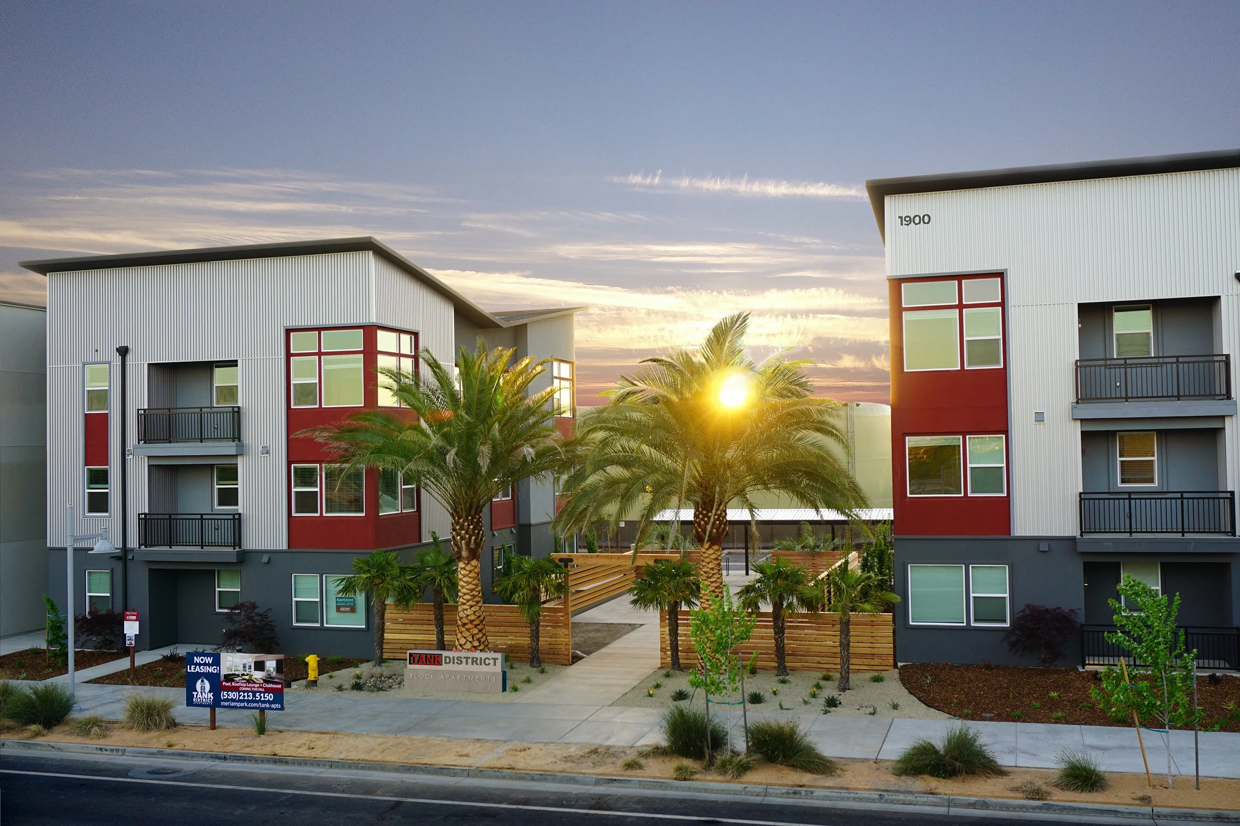 Modern apartment buildings with palm trees at sunset, featuring balconies and large windows.