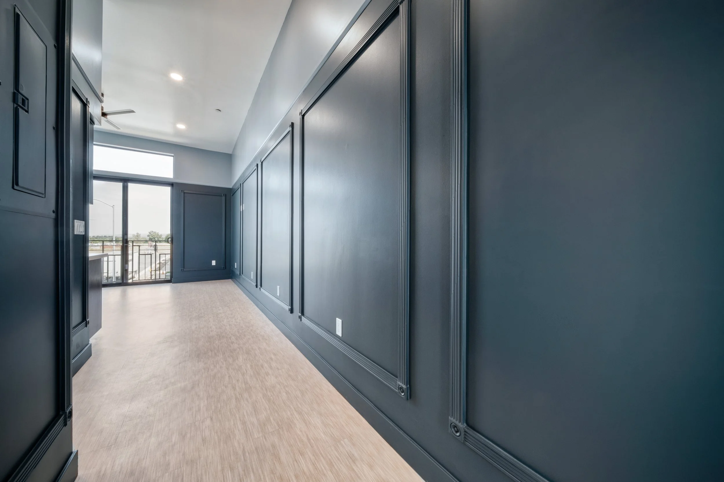 Empty hallway in a modern apartment with dark walls, large window, and light wood flooring.
