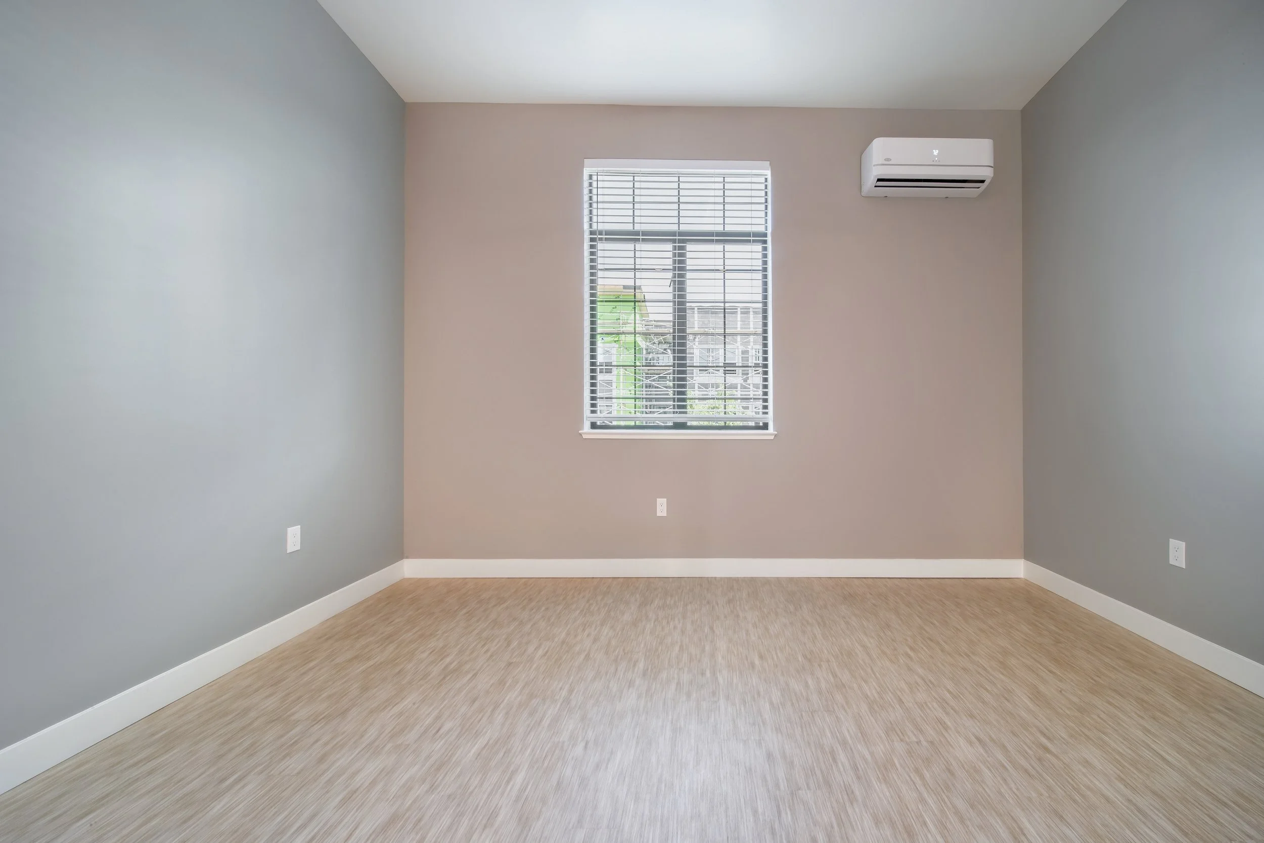Empty room with beige carpet, pale pink and gray walls, a window with blinds, and an air conditioning unit.