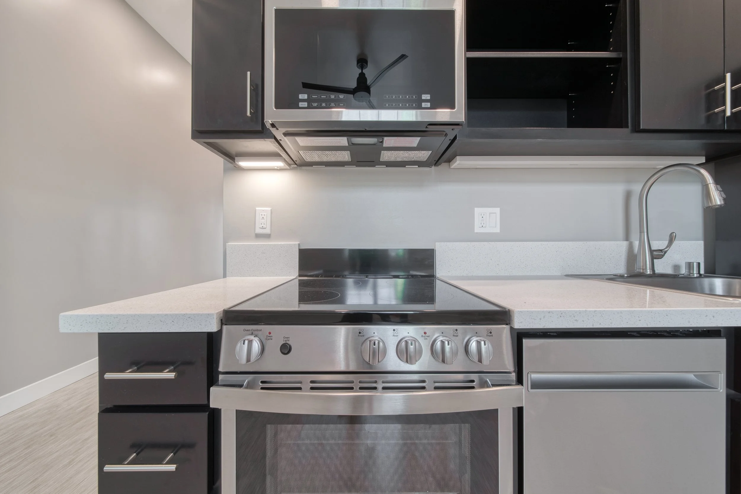 Modern luxury kitchen with a stainless steel stove, black microwave above, gray cabinets, and a white speckled countertop with an integrated sink.