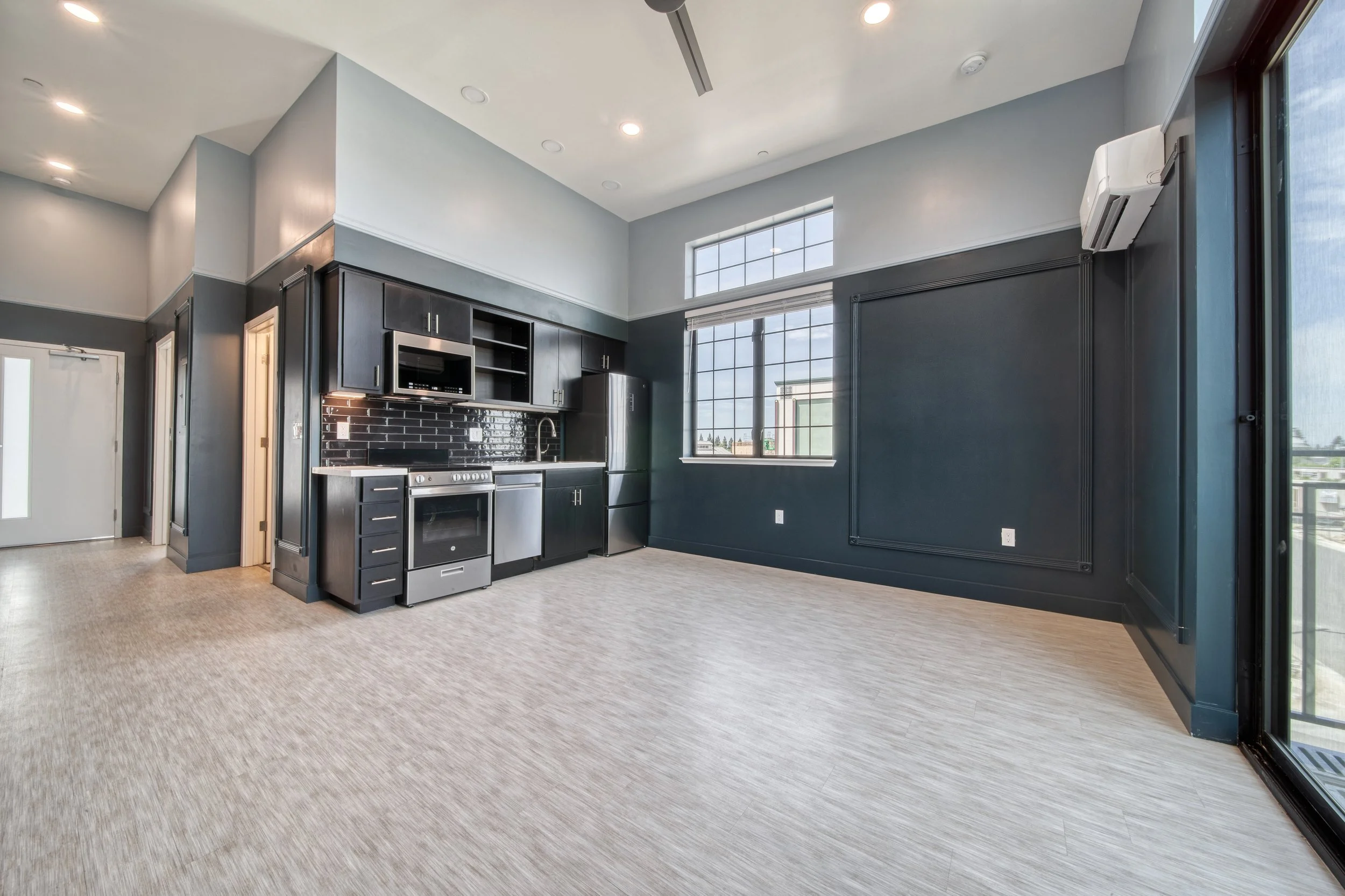 Empty kitchen and dining area with dark cabinets, stainless steel appliances, and large windows.