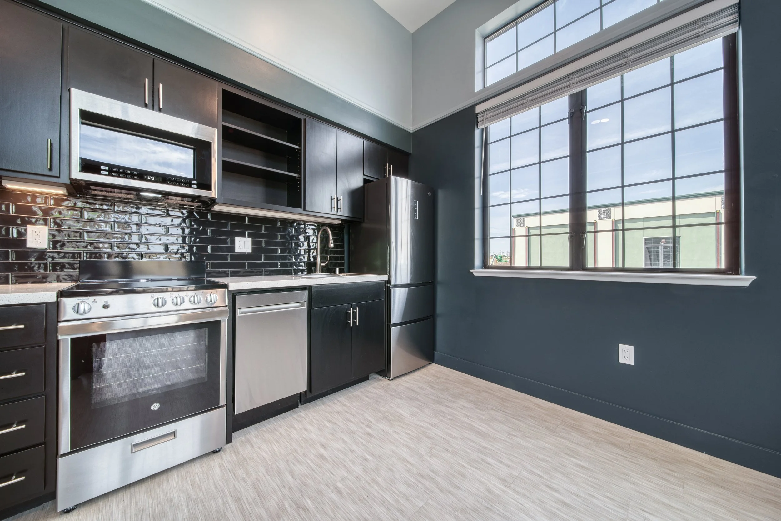 Modern kitchen with black cabinets, stainless steel appliances, black subway tile backsplash, and large window
