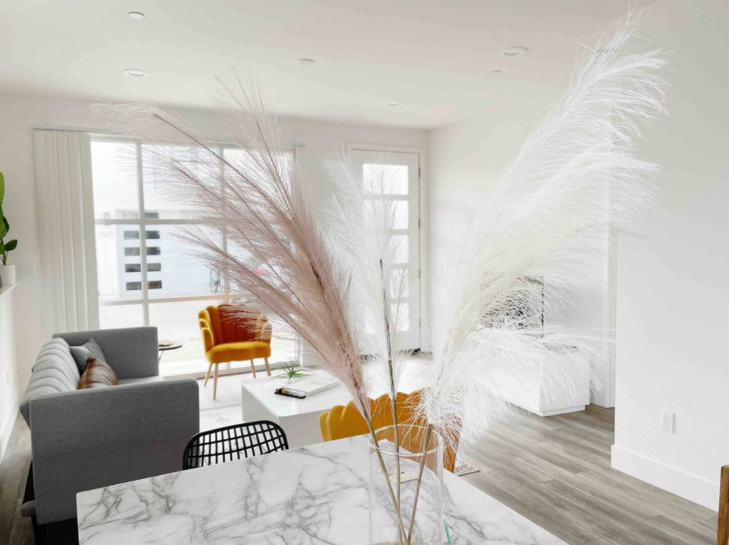 Living room with gray sofa, yellow armchair, white coffee table, and tall white and pink pampas grass in a vase on a marble countertop.