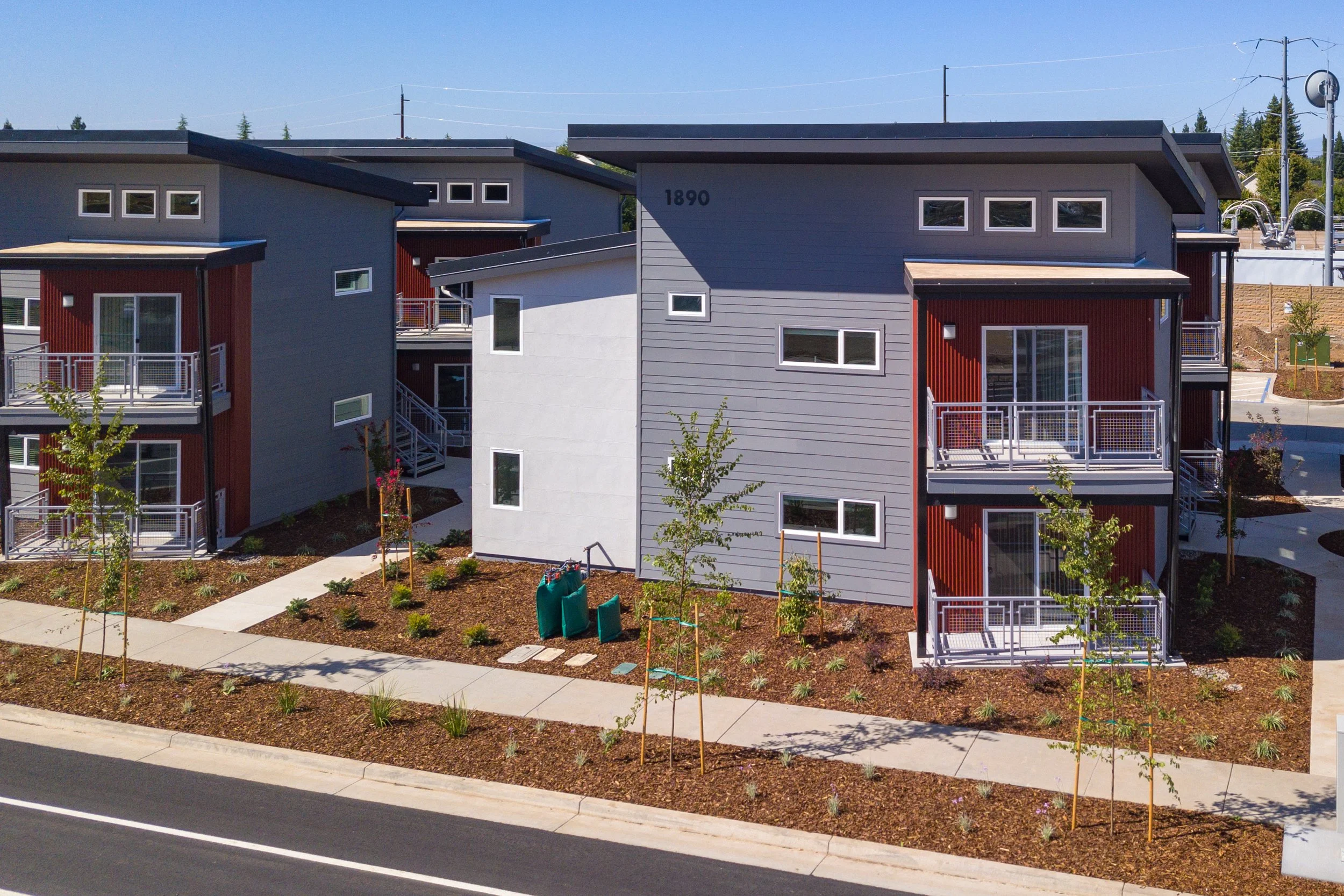 New modern apartment buildings with gray and red exteriors, surrounded by landscaped gardens and walking paths.