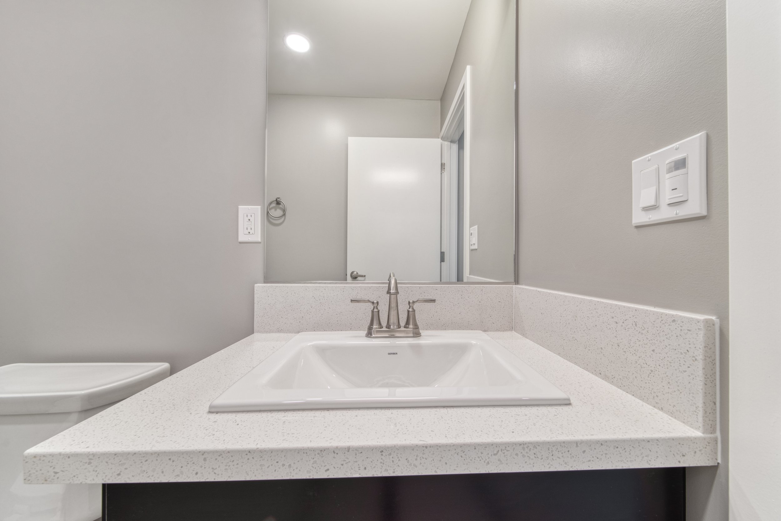 Bathroom vanity with a white sink, faucet, and large mirror, light grey walls, and a doorway in the background.