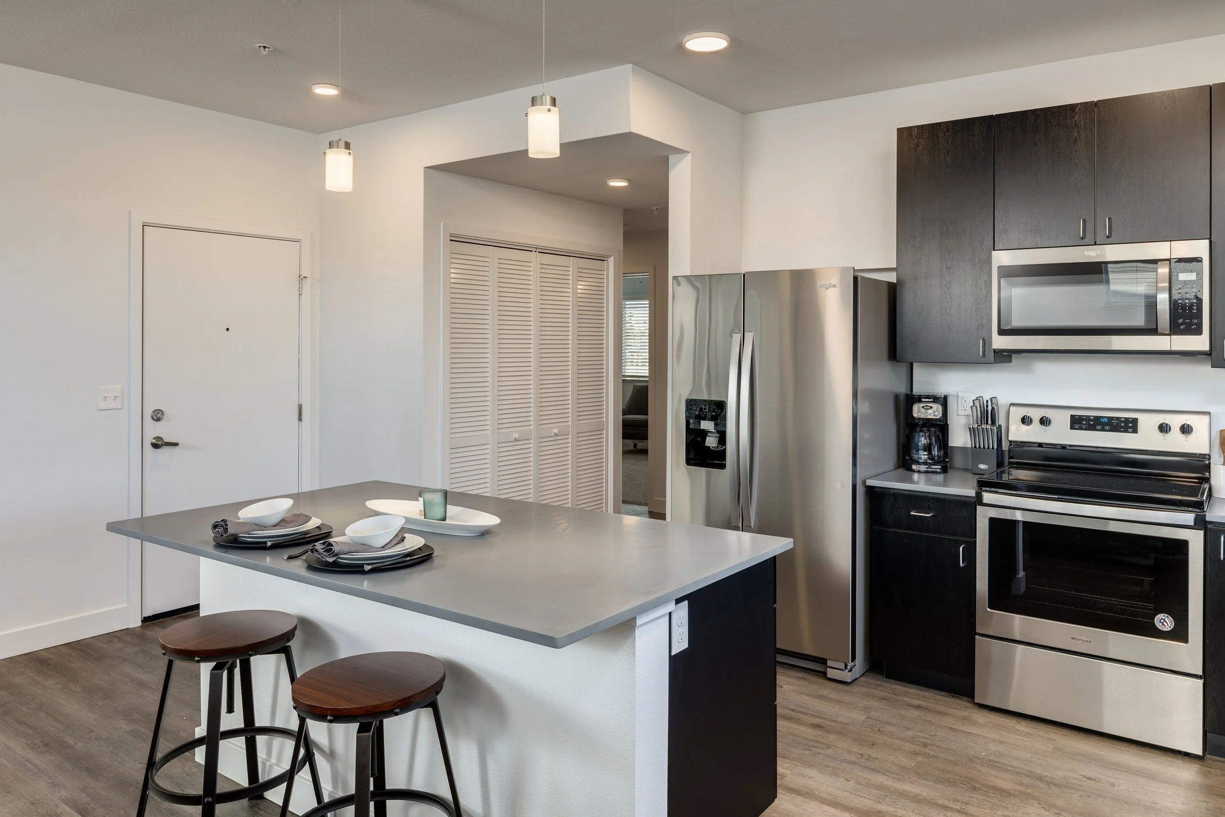 Modern kitchen with stainless steel appliances, black cabinets, a kitchen island with place settings, and a hardwood floor.