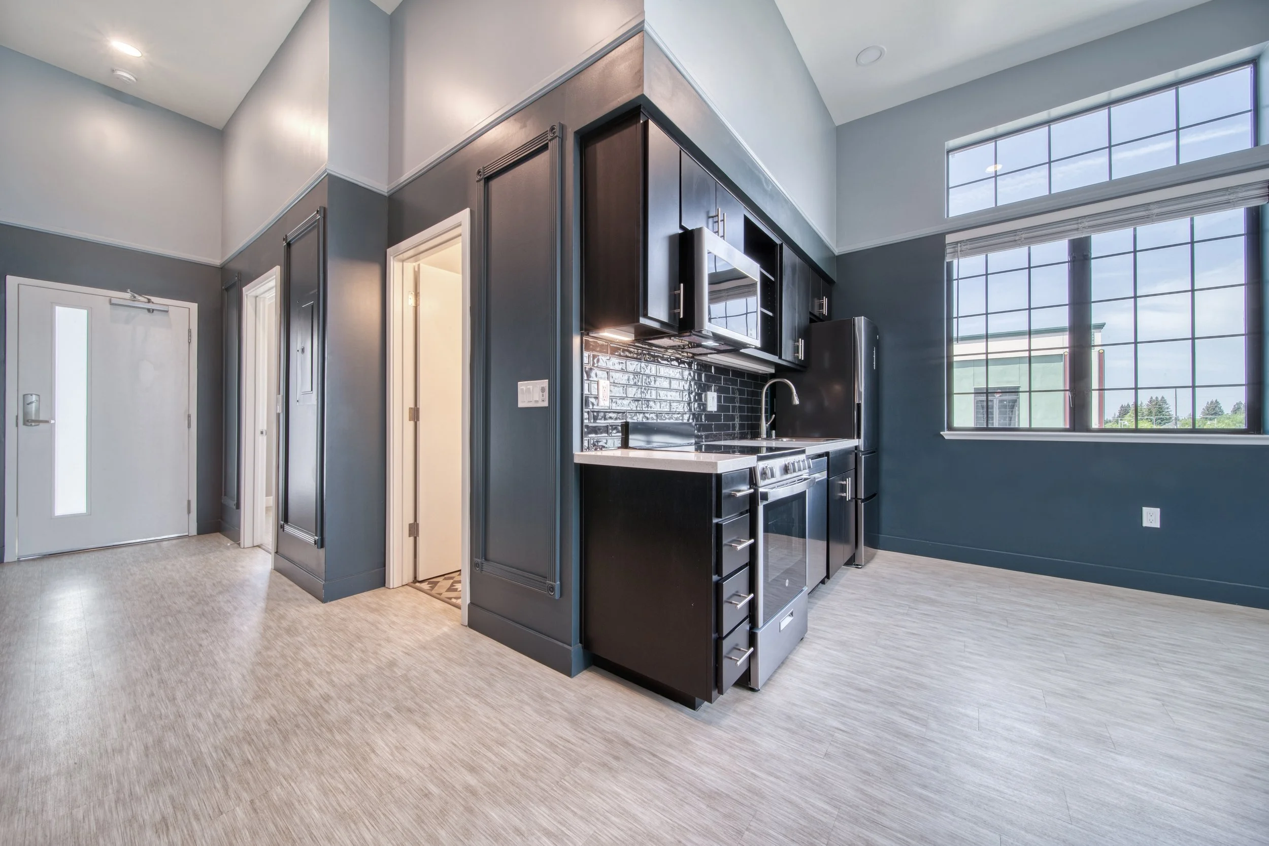 Modern kitchen with dark cabinets, white countertops, stainless steel appliances, large window, and gray walls.