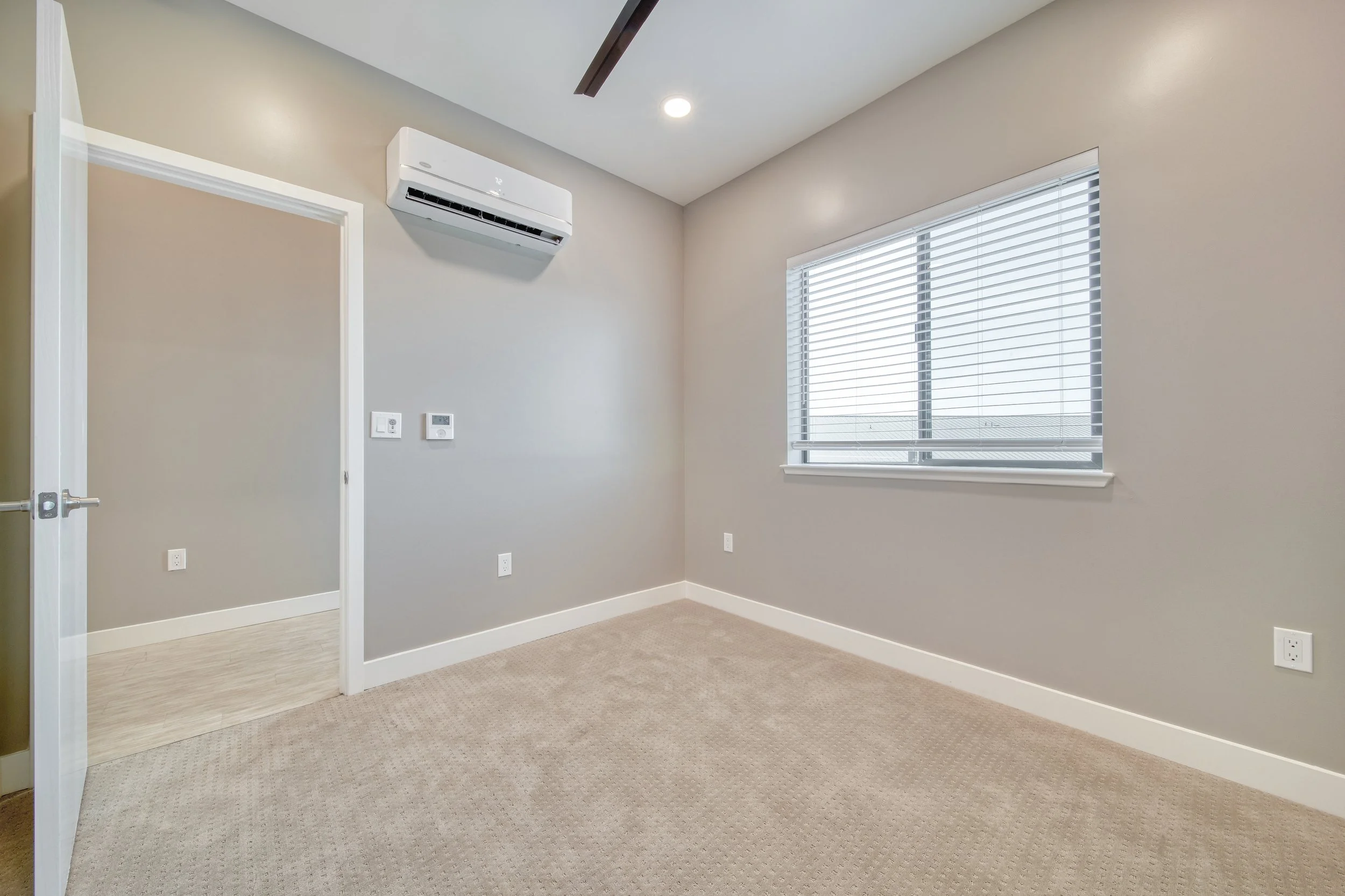 Empty room with beige carpet, light gray walls, a window with blinds, an air conditioning unit, and a doorway