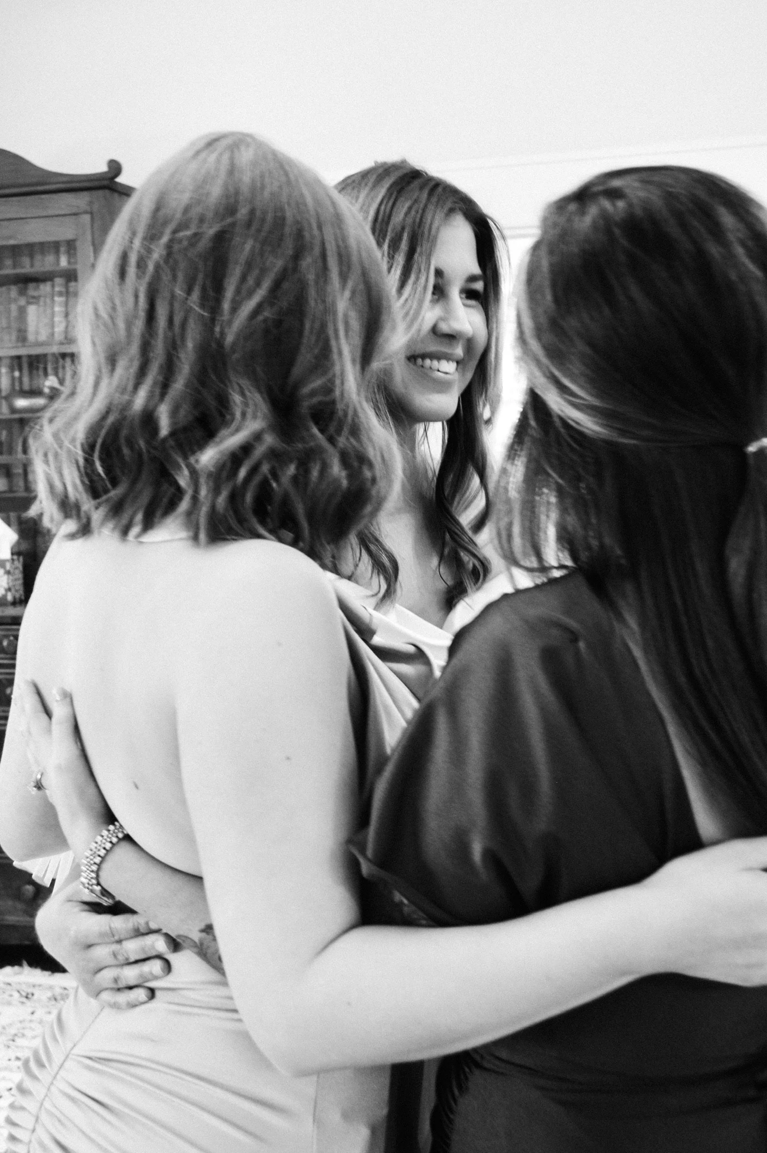 Three women embracing and smiling at each other indoors.