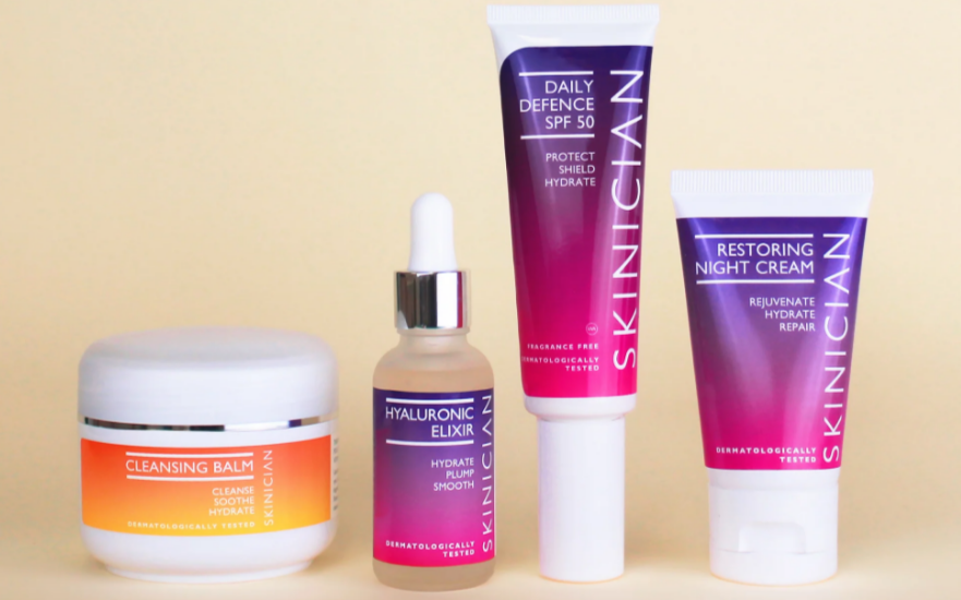 Four skincare products: a cleansing balm jar, hyaluronic elixir in a dropper bottle, daily defense SPF 50 in a tube, and restoring night cream in a tube, all labeled SKINICIAN.
