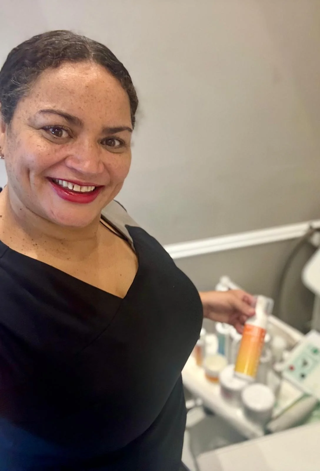 A woman smiling at the camera, holding a pill bottle, in a medical or pharmacy setting.