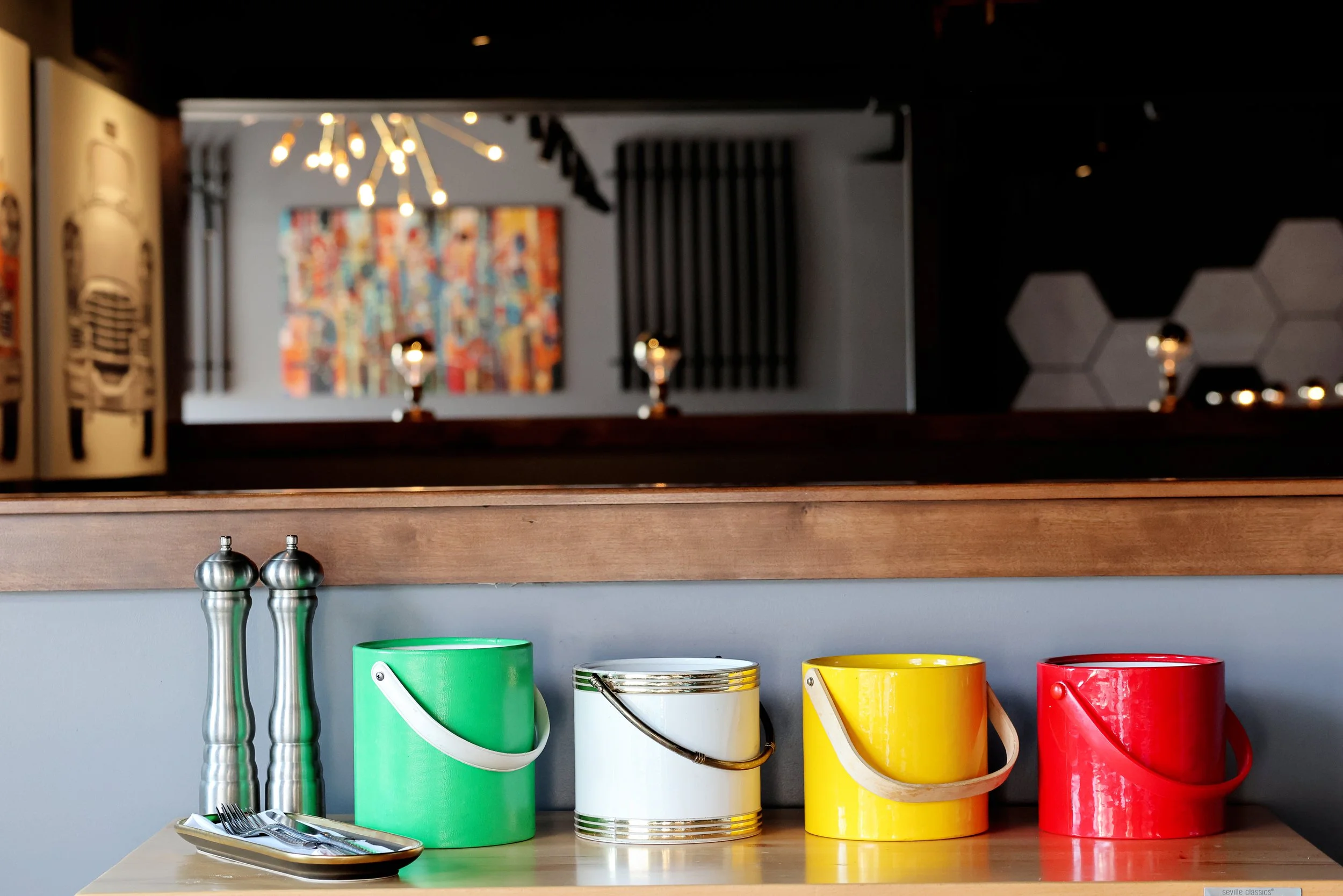 Colorful tin cans in green, white, yellow, and red on a wooden counter with salt and pepper shakers and a plate of forks and knives.