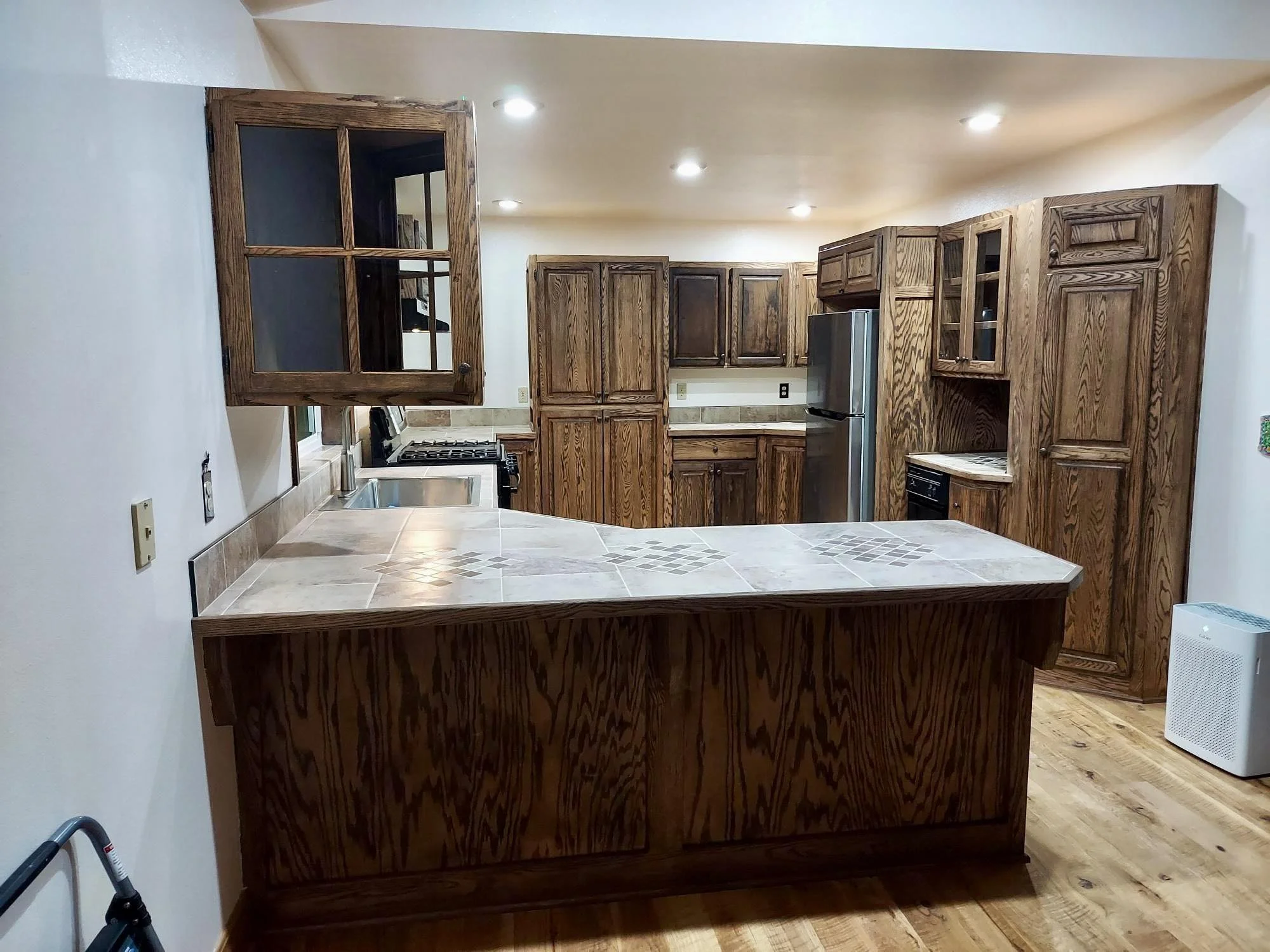 Kitchen with wooden cabinets and granite countertops, stainless steel refrigerator, and tile flooring.
