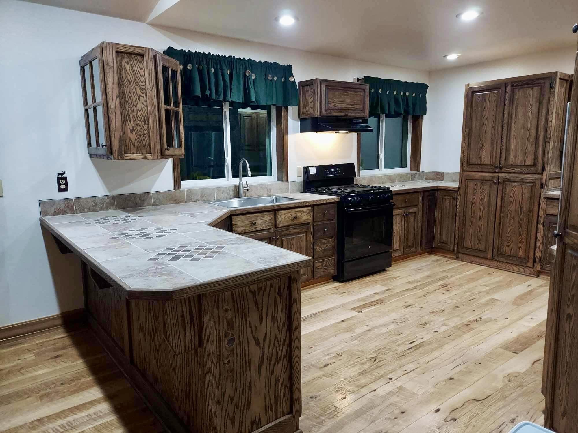 Finished kitchen remodel with wood cabinetry, tile countertops, hardwood flooring, and interior finish work.