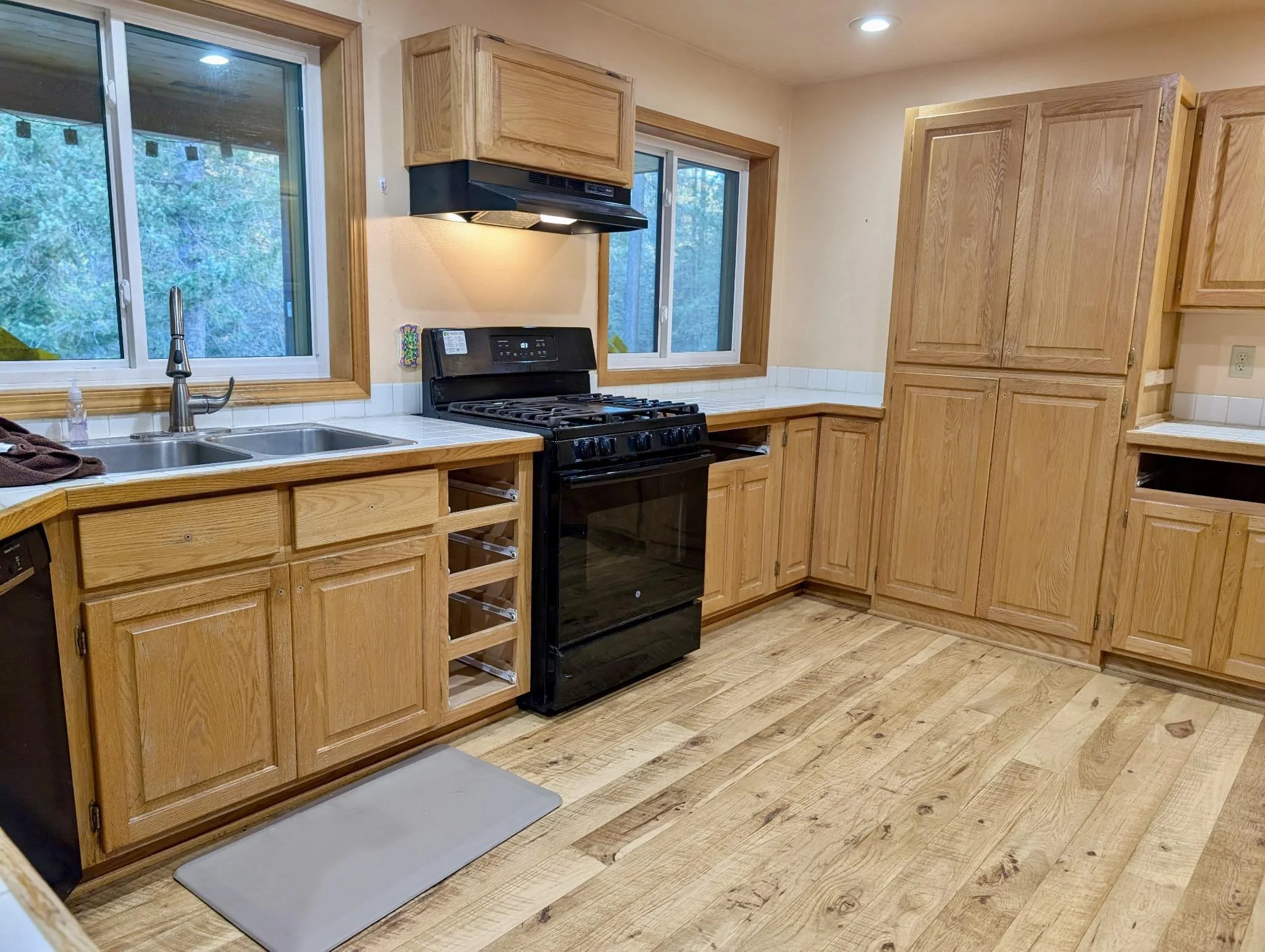 Kitchen remodel with wood cabinets, black stove, sink, large windows, and updated flooring.