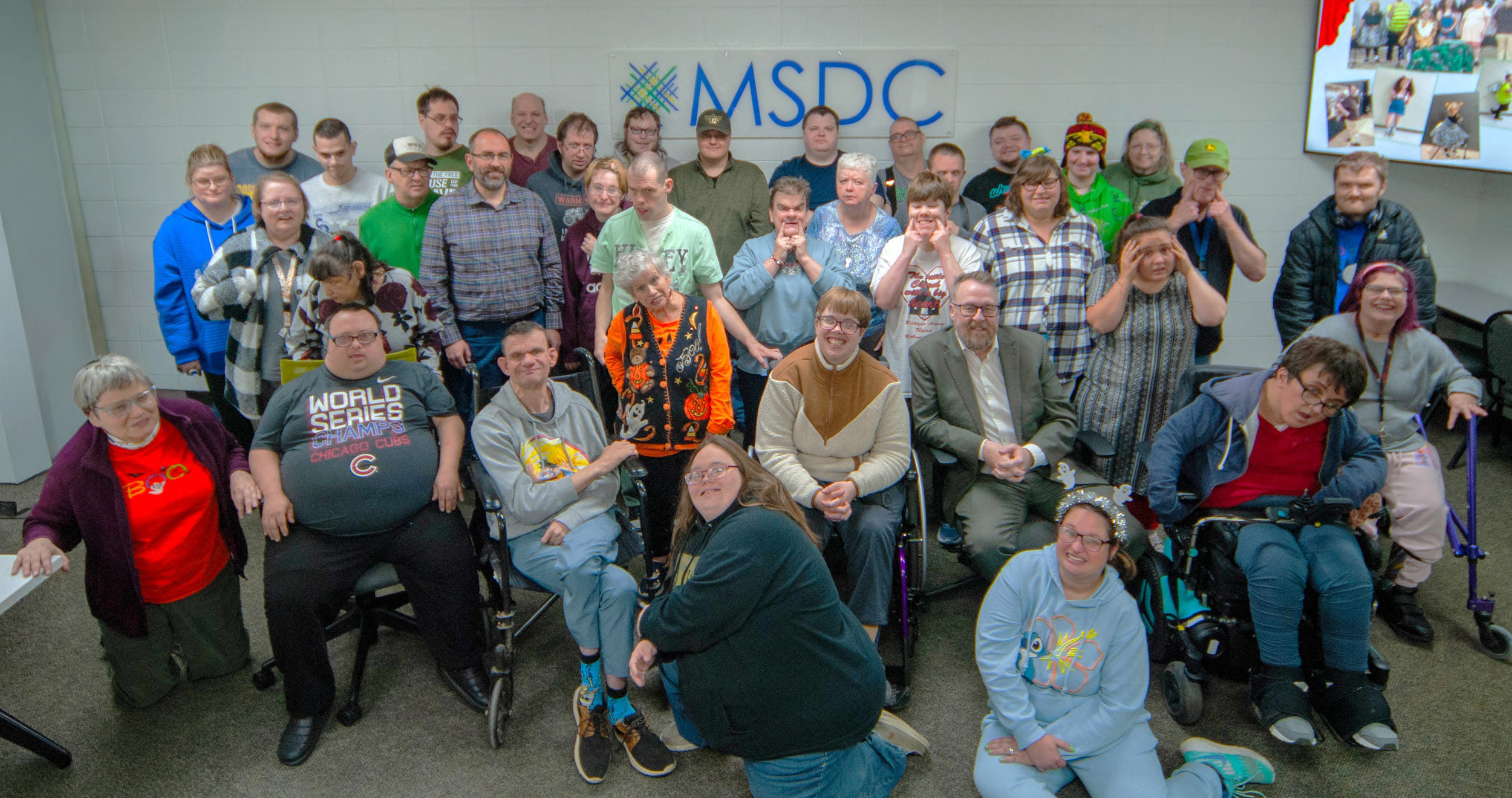 Adults with disabilities and MSDC leadership, including the CEO and COO, posing together in a group photo in front of a wall with the MSDC logo, in an indoor setting.
