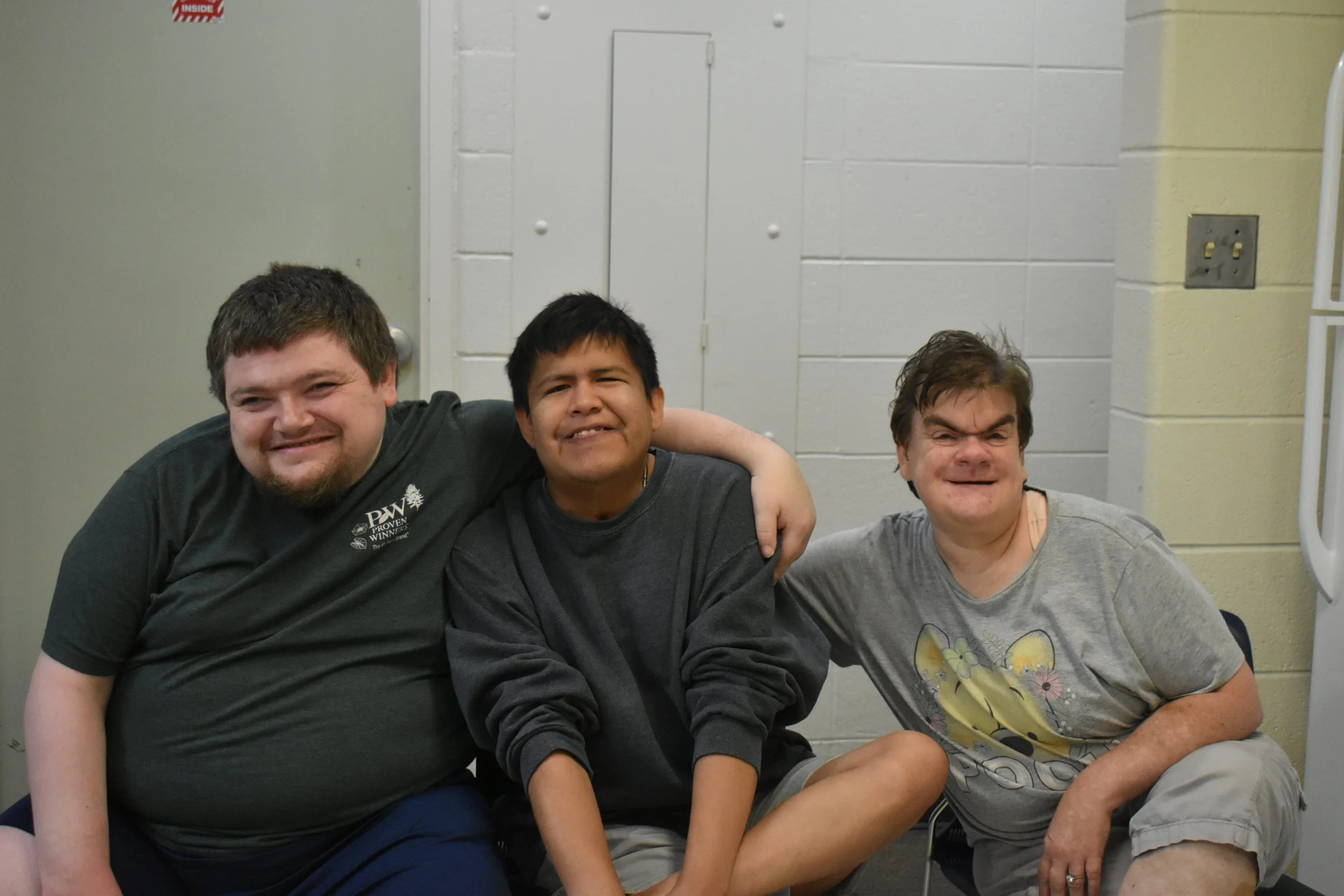 Three men sitting together in a room, smiling with their arms around each other.