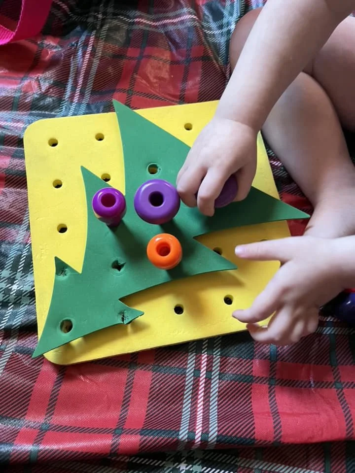 Child playing with a colorful wooden pretend food set on a tablecloth with a red, black, and white plaid pattern.
