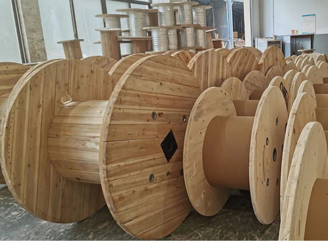 Large wooden spools used for wire manufacturing in a workshop, with spools arranged in rows.