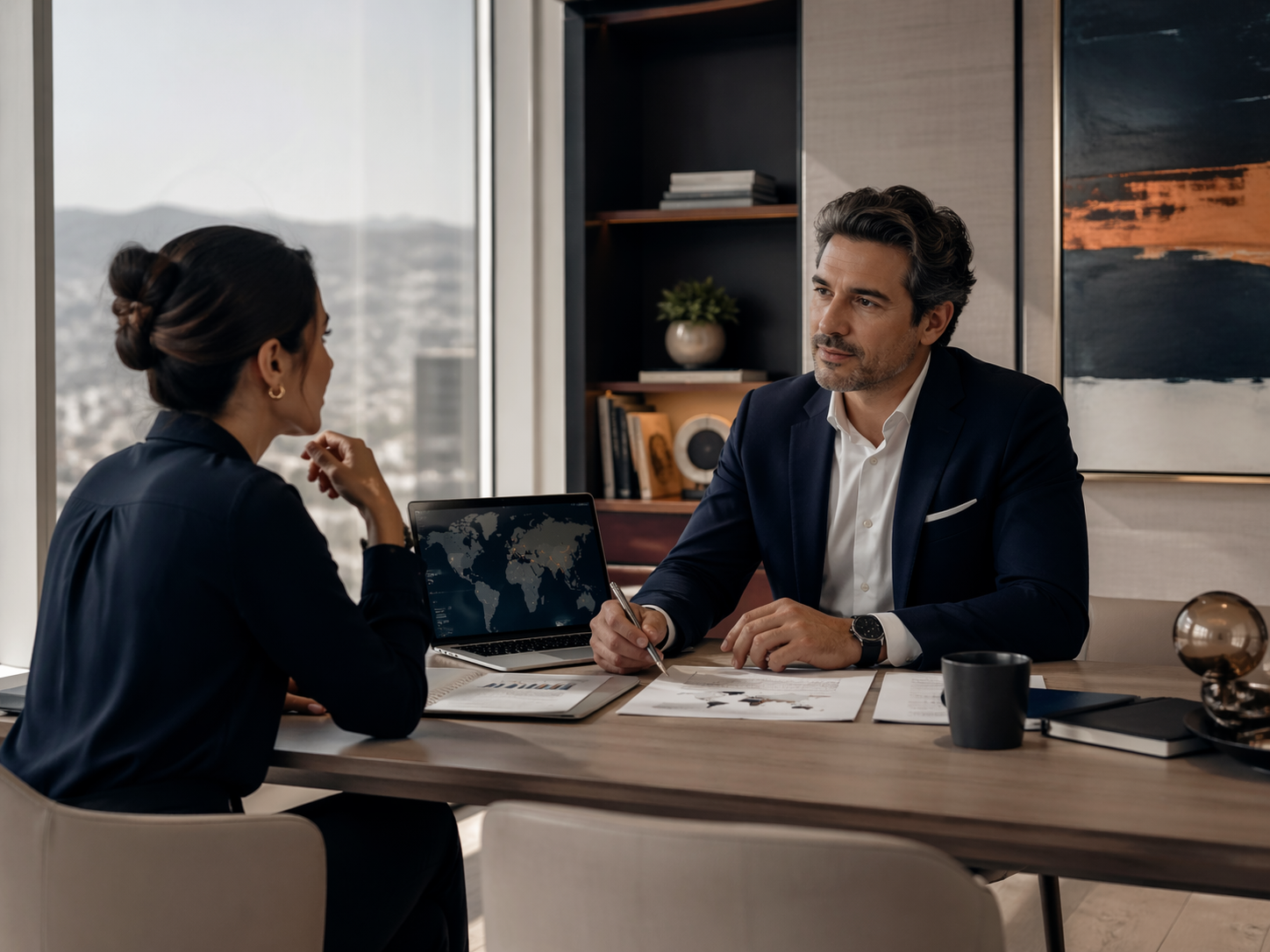Two professionals meeting in an office with documents, a laptop, and a city view.