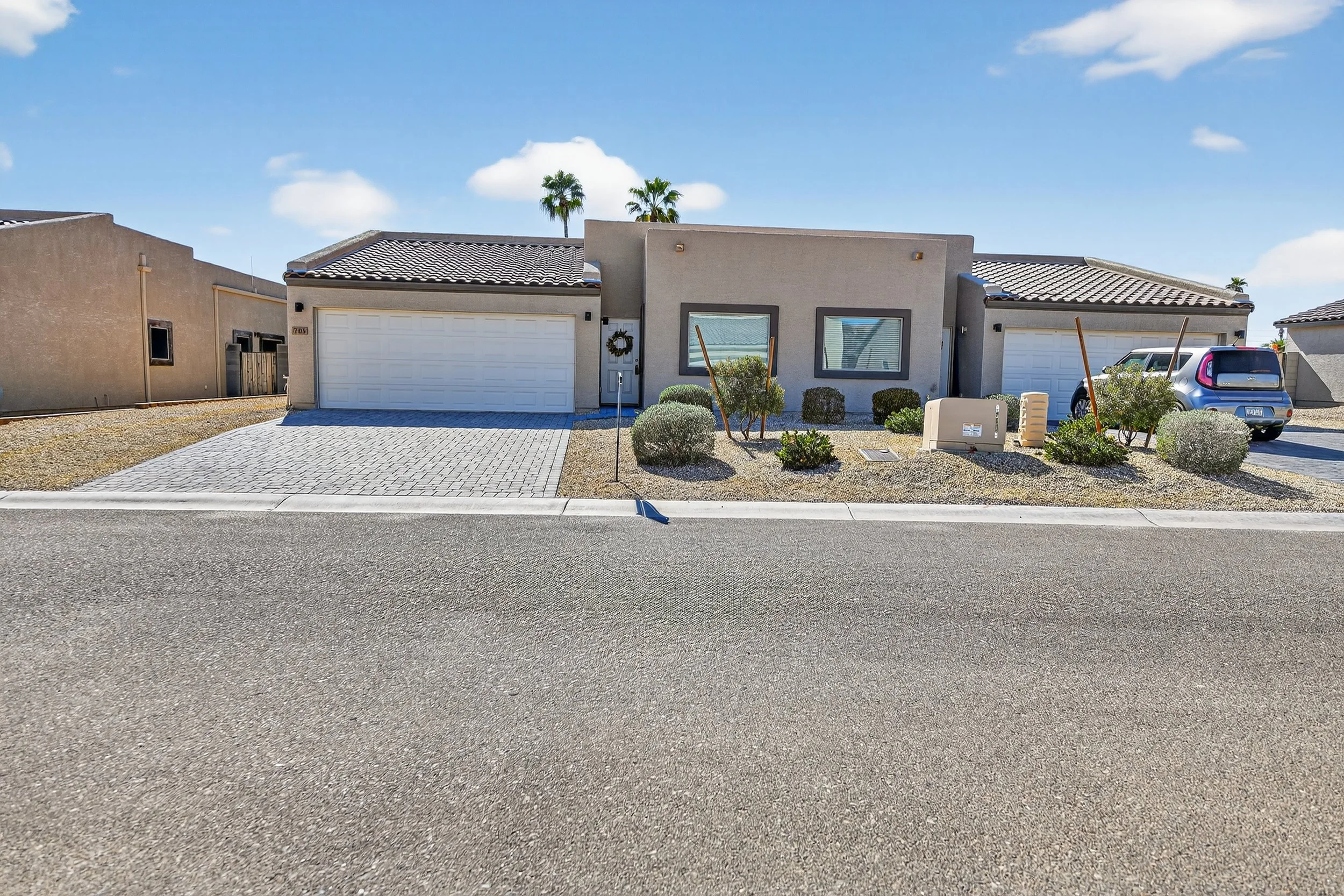 A modern house with two garage doors, desert landscaping, and a clear blue sky with some clouds.