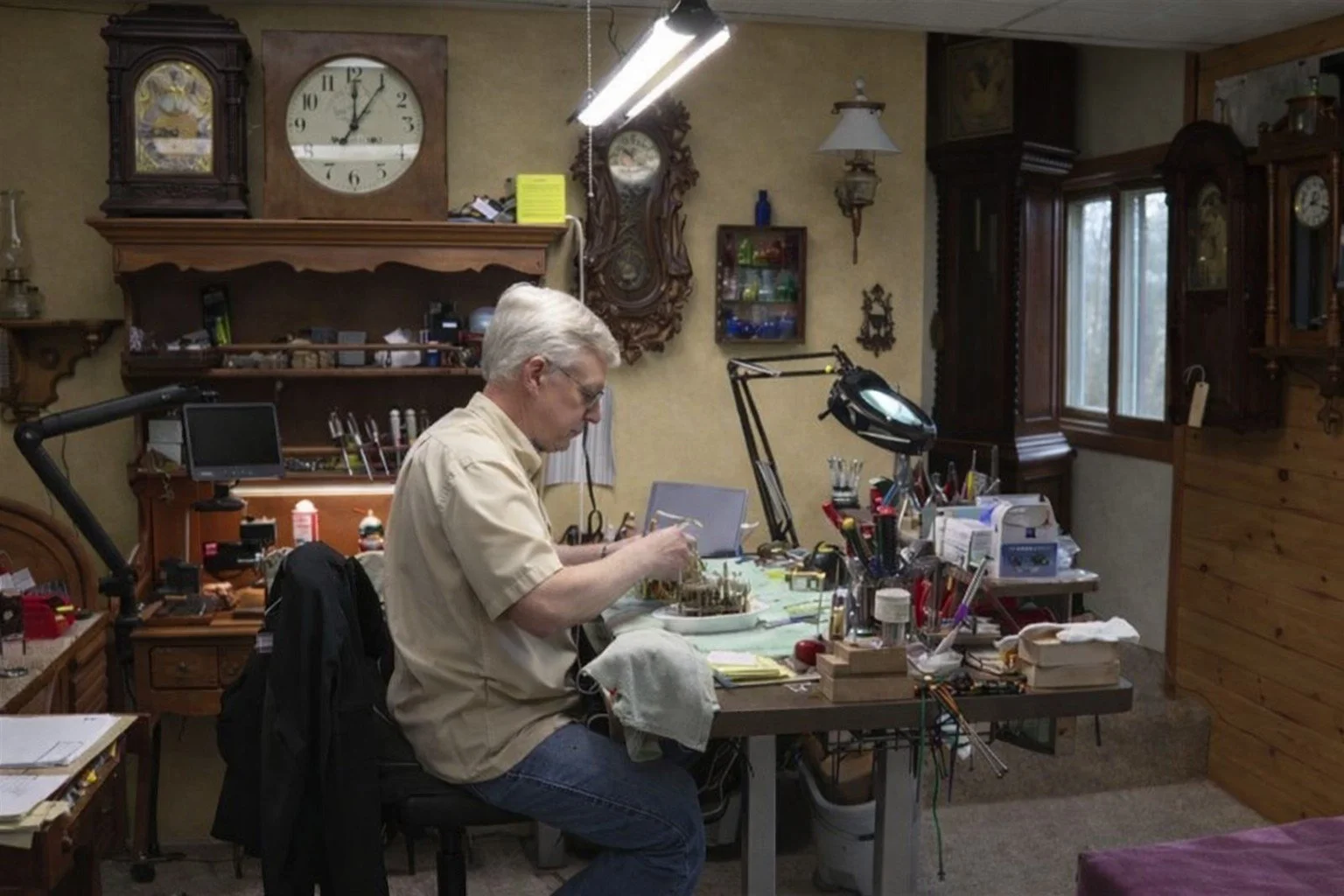 A professional clock repair person repairing clocks at his desk.