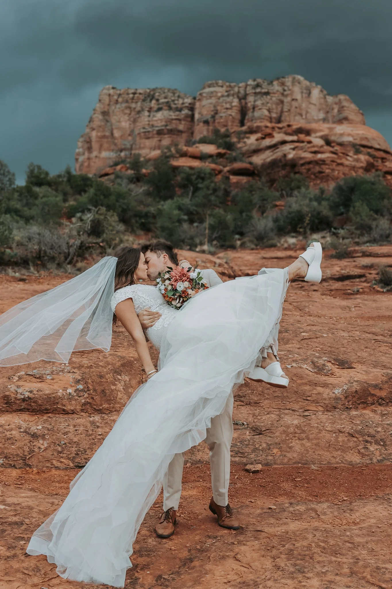 Romantic Sedona elopement on the red rocks with bride lifted in front of scenic desert cliffs.